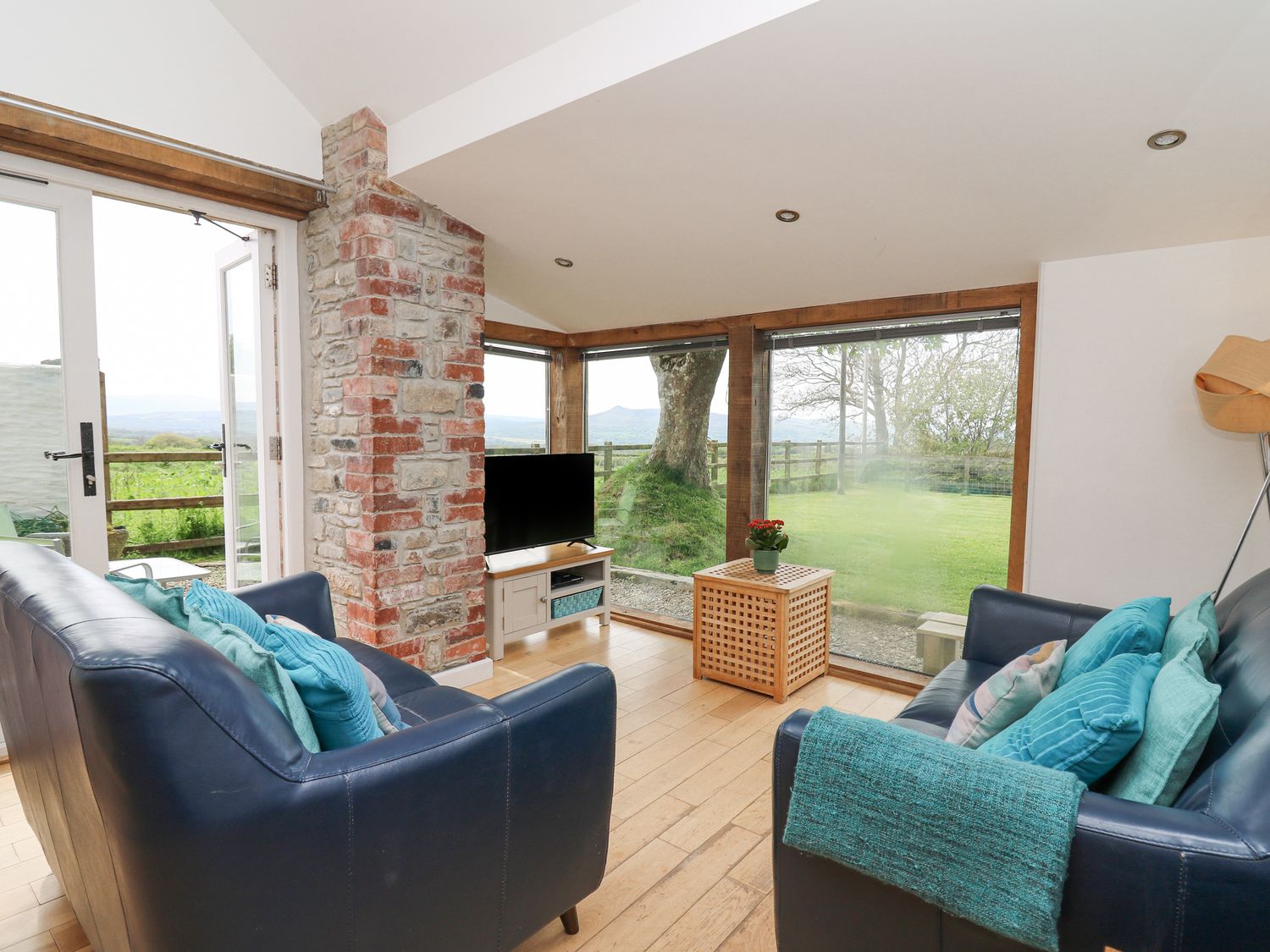 A living room with two blue sofas a small wooden table a television and large windows overlooking a garden at Y Cartws in Newport