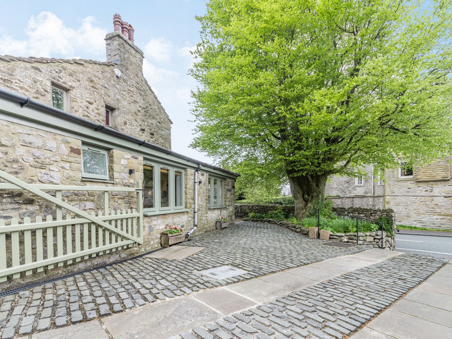 A stone cottage with a cobblestone pathway and a large tree at The Friendly Room in Austwick