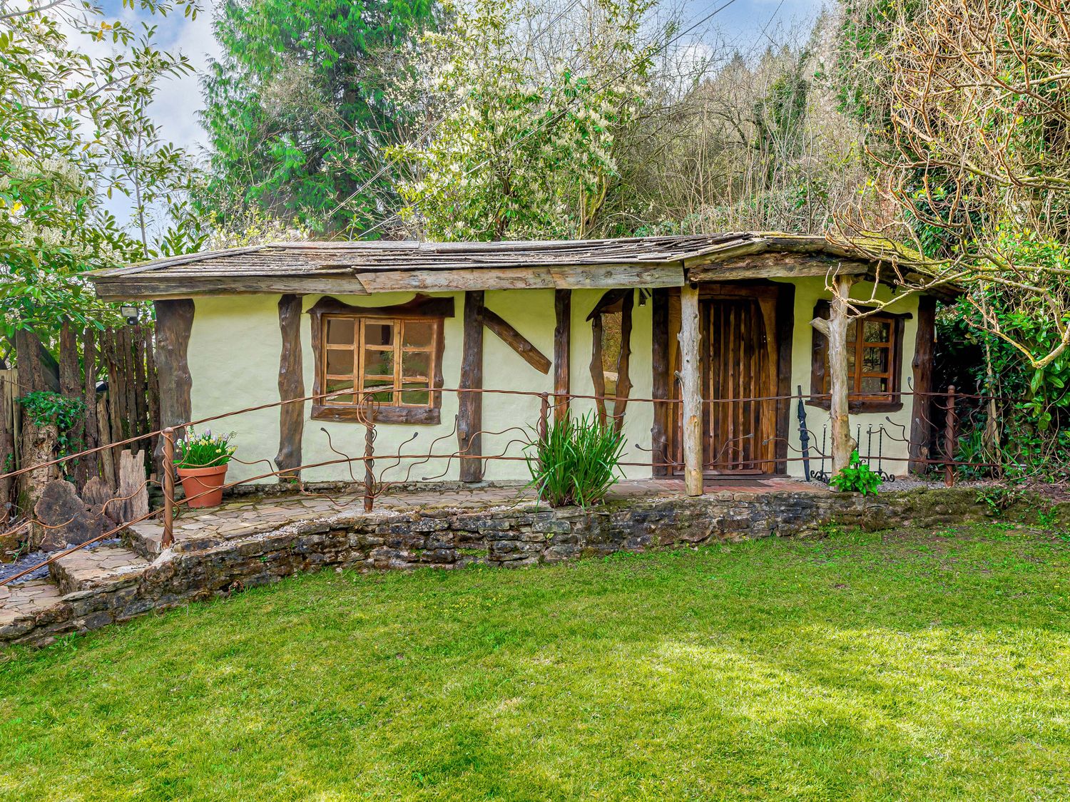 A small rustic house with wooden beams windows and a door surrounded by greenery and a grassy lawn at Brookbank Folly in Mitcheldean