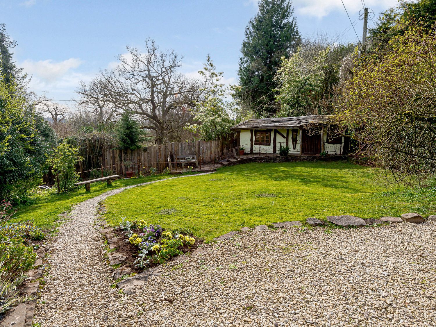 A garden with a gravel path a small wooden bench flowers a lawn and a timber framed shed at Brookbank Folly in Mitcheldean