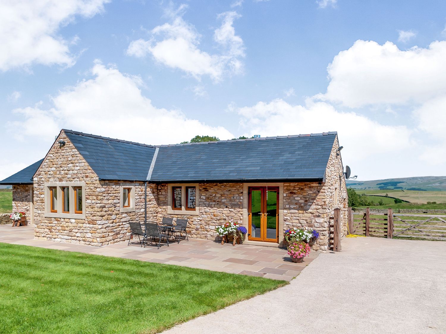 A stone cottage with slate roof and patio furniture on a paved area at Routster Cottage in Settle Three Peaks Country