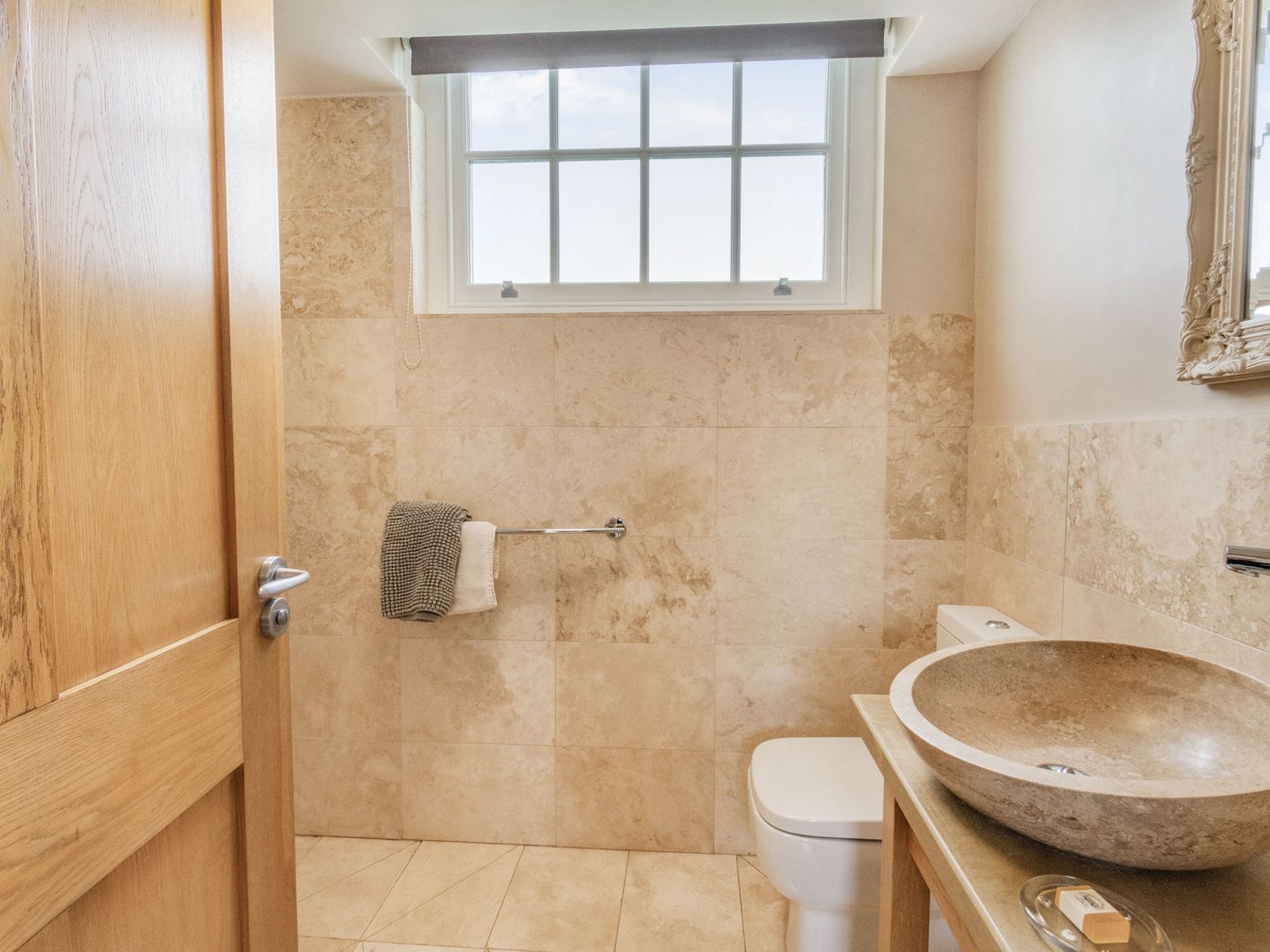 A bathroom with a stone sink on a wooden vanity a toilet a towel rack with towels and a window at The Old Chapel in Hornsea