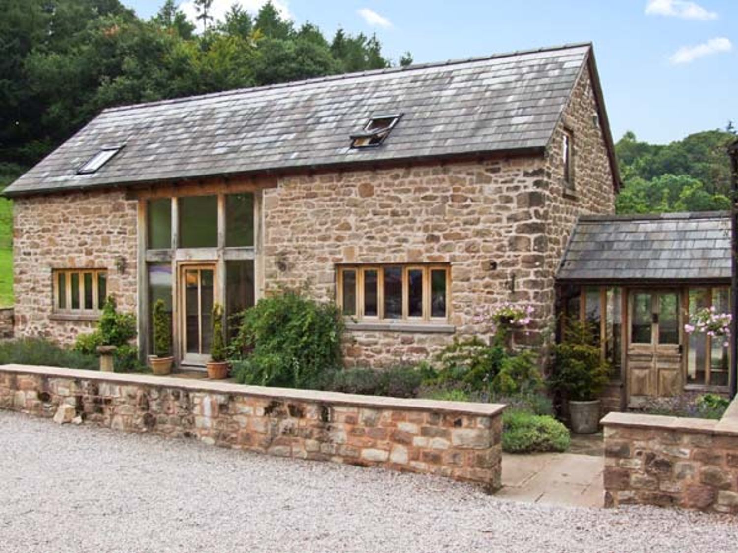 A stone house with a slate roof surrounded by plants and trees at The Lodge Farm Barn in Deepdean near Ross-on-Wye