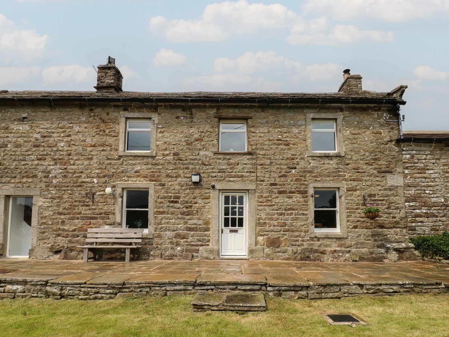An exterior view of a stone house with a bench at High Smarber in Low Row near Reeth