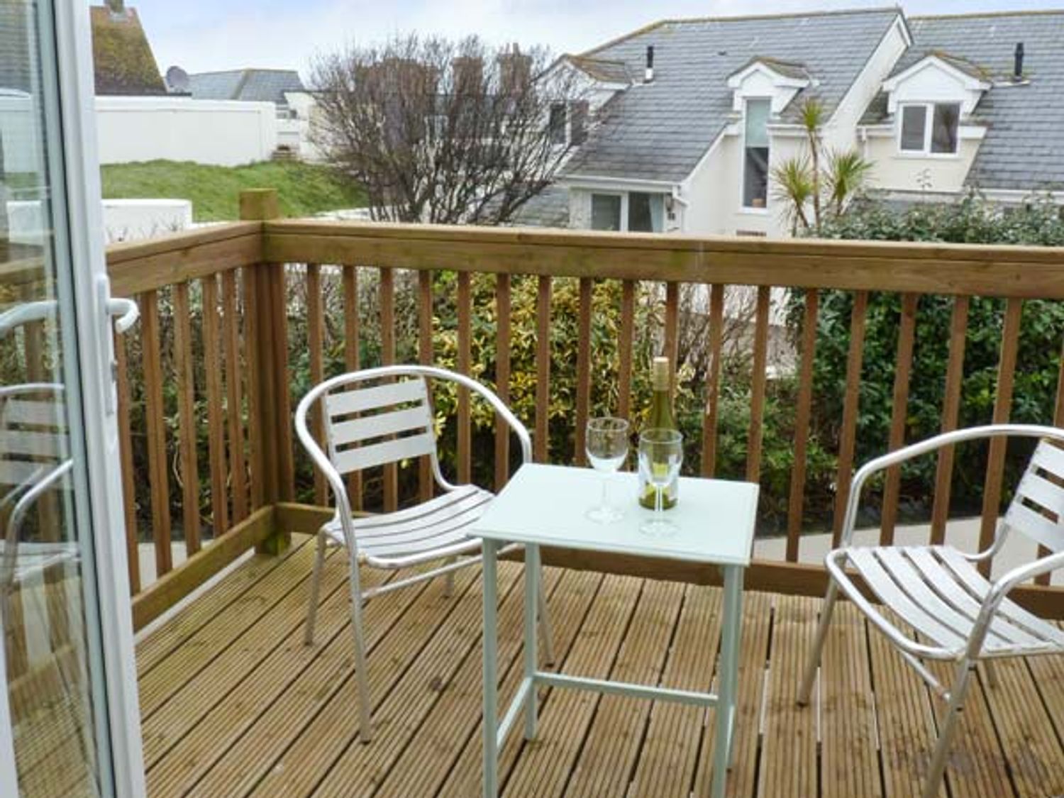 A wooden balcony with two metal chairs and a small table with a bottle and two glasses at Beachcombers in Porth