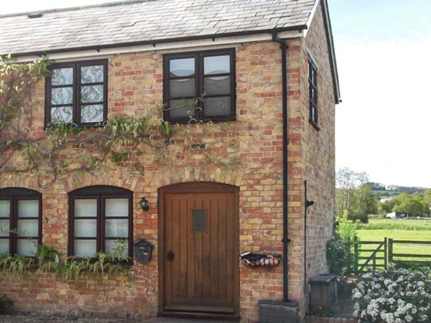 The exterior of a brick house with a wooden door windows and climbing plants at Bluebell Cottage in Newnham-on-Severn near Gloucester