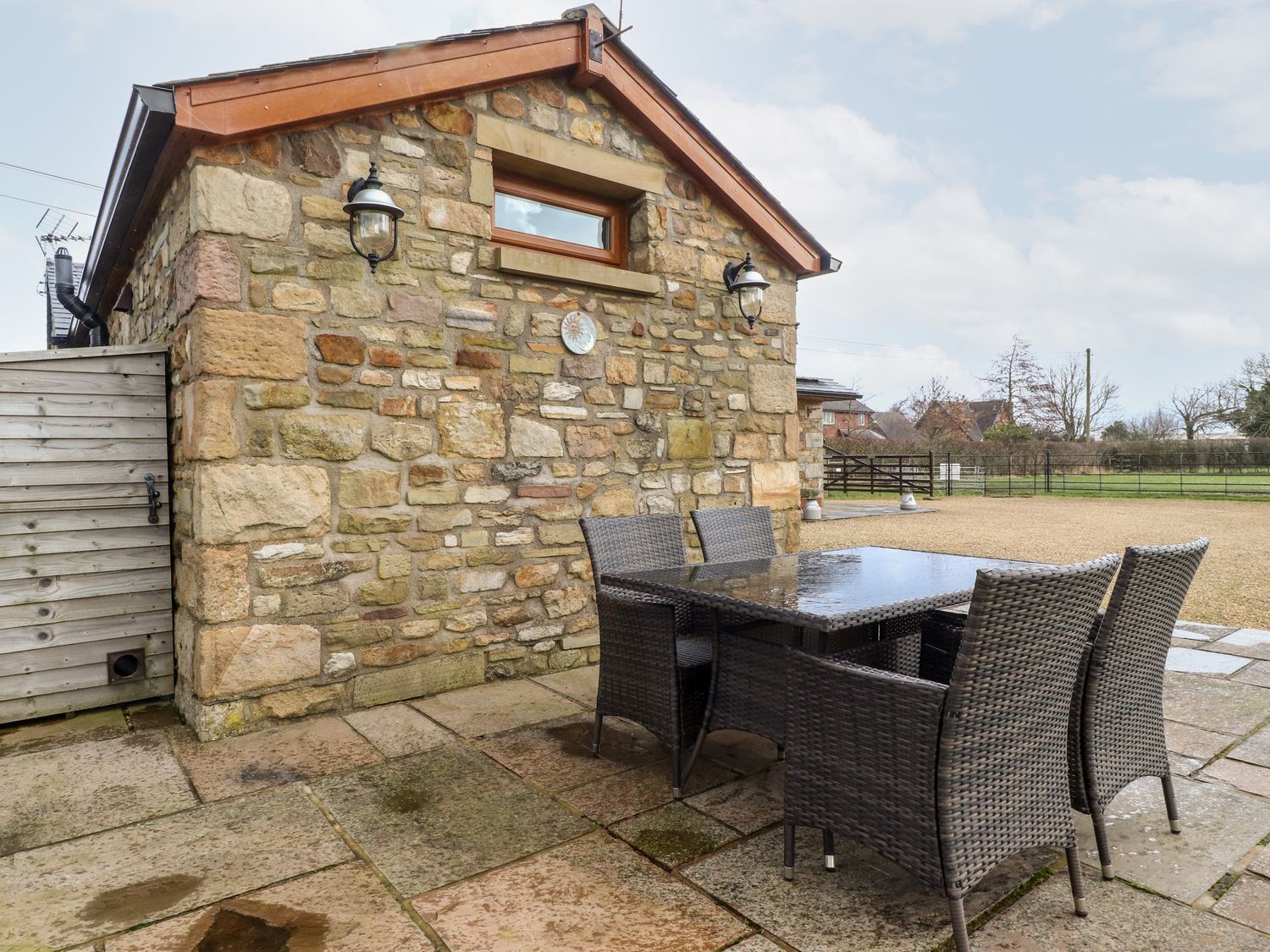 An outdoor patio with a stone wall building and a glass top table with wicker chairs at Deekswood in Pilling near Blackpool