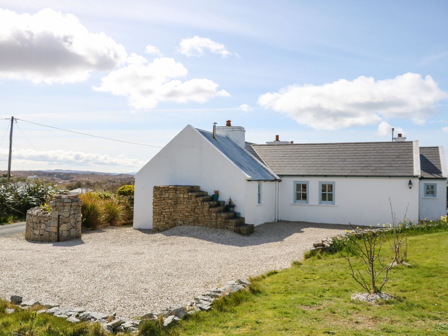 A white house with blue window frames a stone well and stone steps in a gravel yard at Radharc na nOilean in Mullaghdoo near Kincasslagh County Donegal