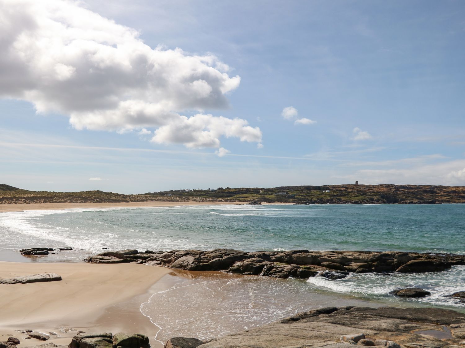 A sandy beach with rocks and waves under a partly cloudy sky at Radharc na nOilean Mullaghdoo near Kincasslagh County Donegal