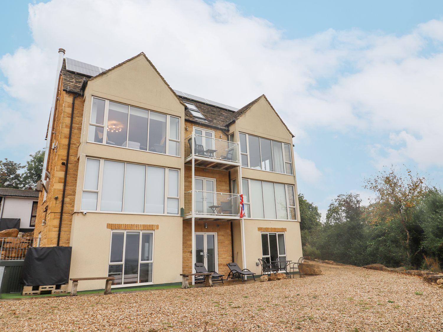 A three-story building with large windows and balconies surrounded by trees at Beautiful Cotswold View in Bourton-On-The-Water