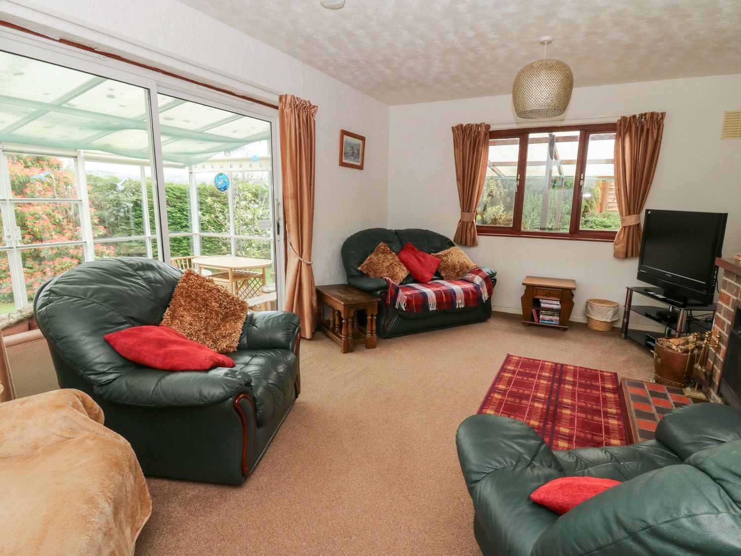 A living room with green leather armchairs a sofa a television and sliding glass doors leading to a conservatory at Bryn yr Haf in Llanfair Clydogau near Lampeter