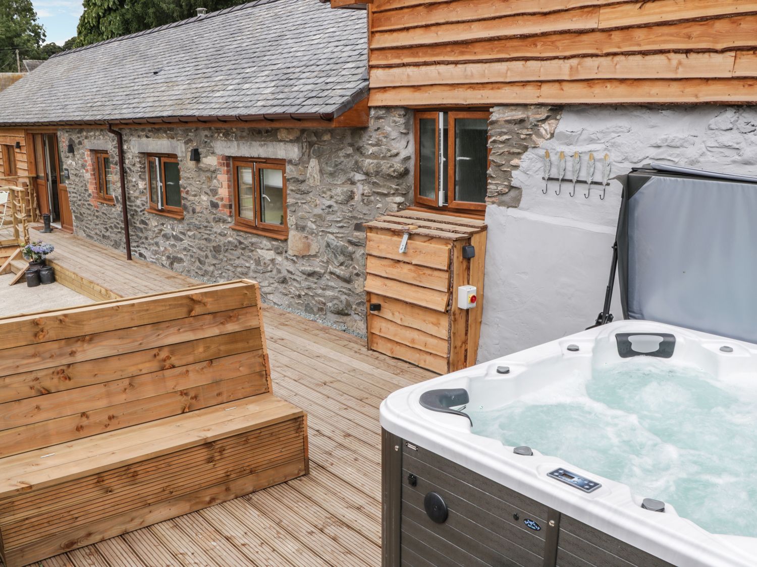 An outdoor deck area with a wooden bench and a hot tub next to a stone and wood building at Rhianwen Plas Moelfre Hall Barns Llanrhaeadr-ym-Mochnant