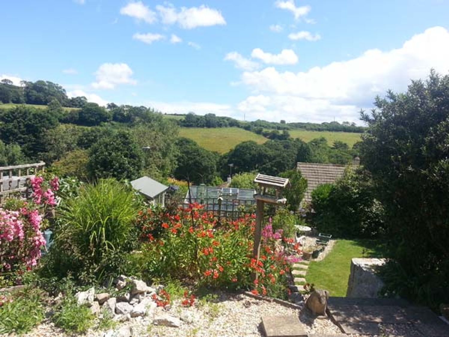 A garden with flowers bushes bird feeder and a seating area overlooking fields and trees at Joylands in Falmouth