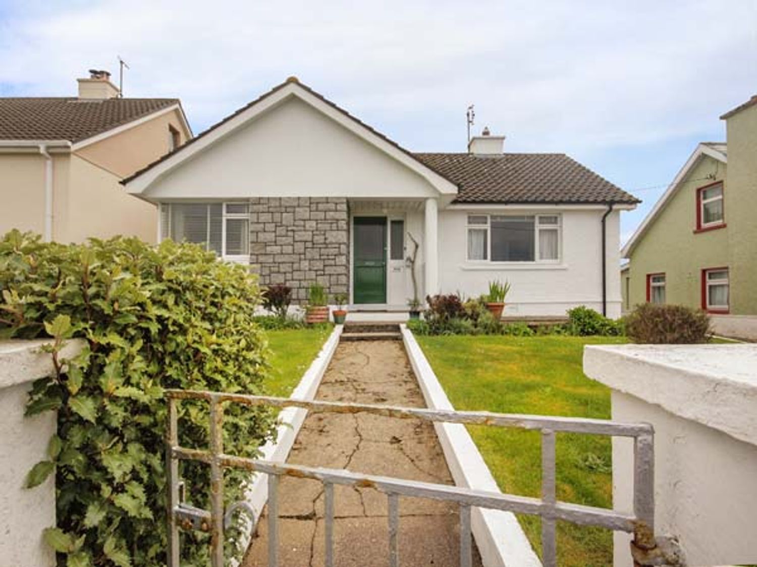 A front view of a single-story house with a green door a concrete walkway and lawn at Teach Annie in Falcarragh County Donegal