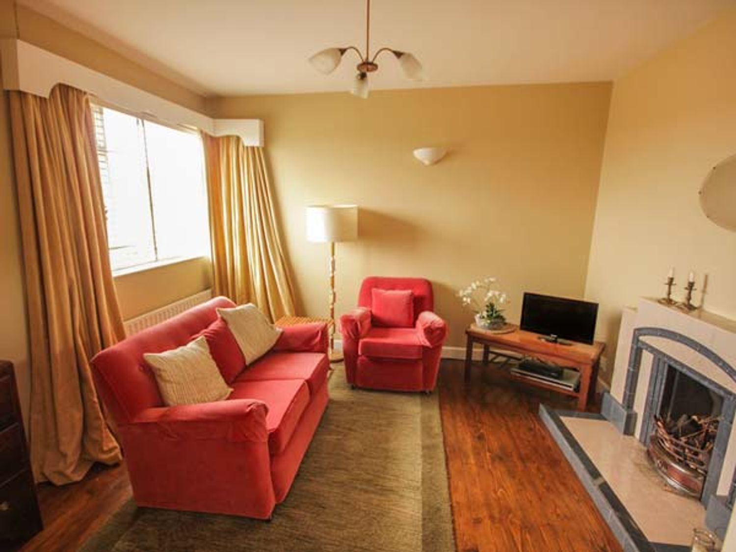 A living room with red sofa and armchair a wooden coffee table TV and a fireplace at Teach Annie in Falcarragh County Donegal