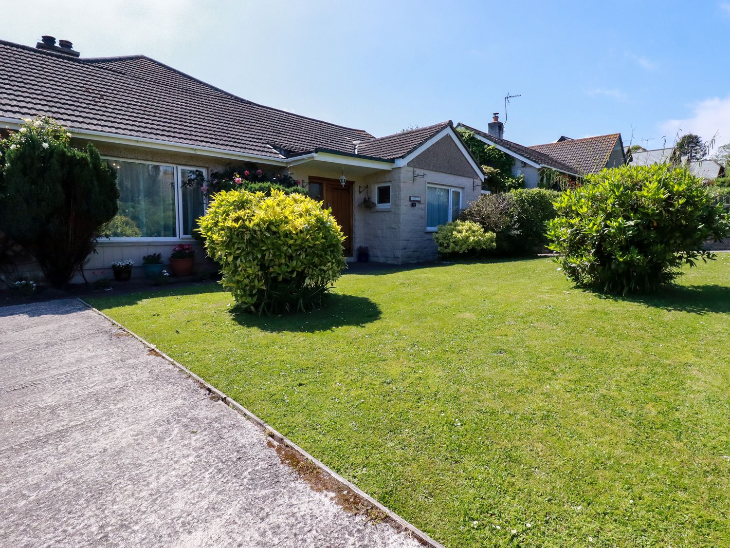 A front view of a single-story house with a tiled roof a lawn with shrubs and a concrete driveway at Summerfield Cottage in Gorran Haven