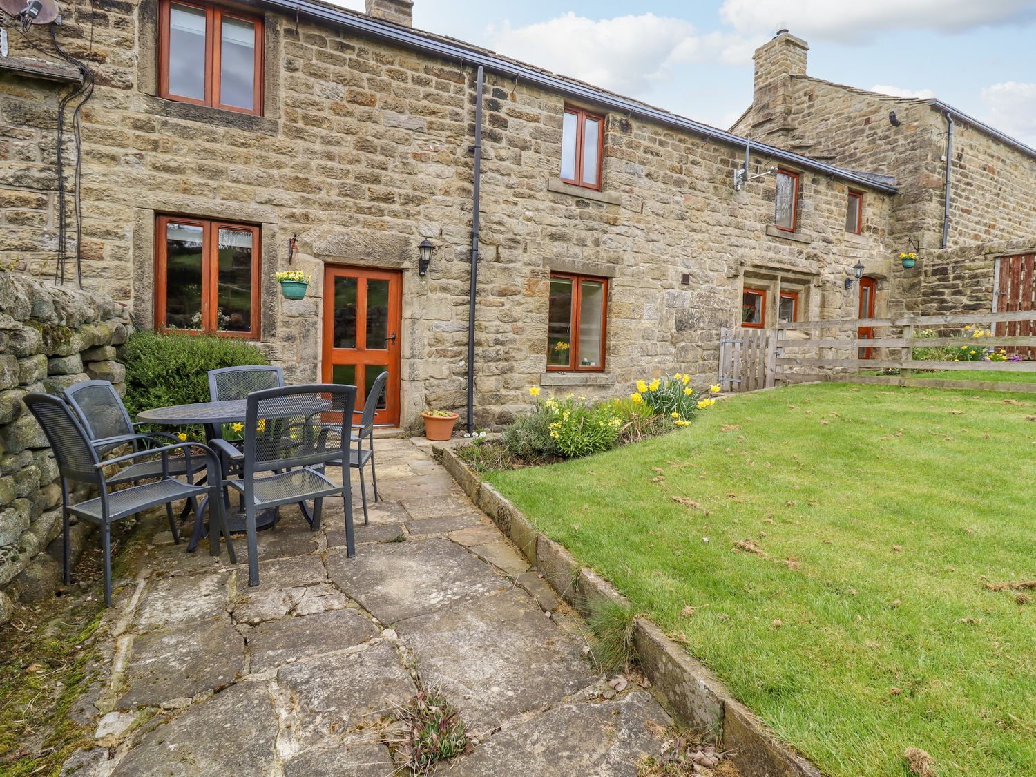 A stone cottage exterior with a paved patio table and chairs and a grassy garden at Curlew Cottage in Silsden