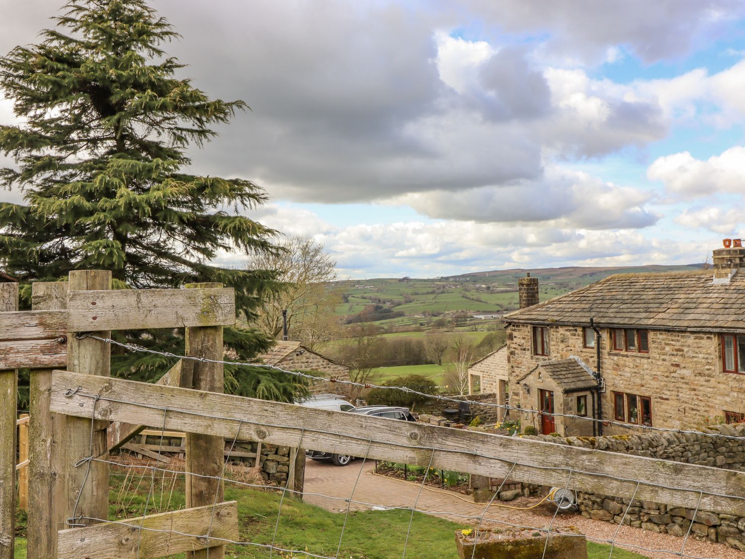 A stone house with a pitched roof near a wooden fence with countryside and hills in the background at Curlew Cottage in Silsden
