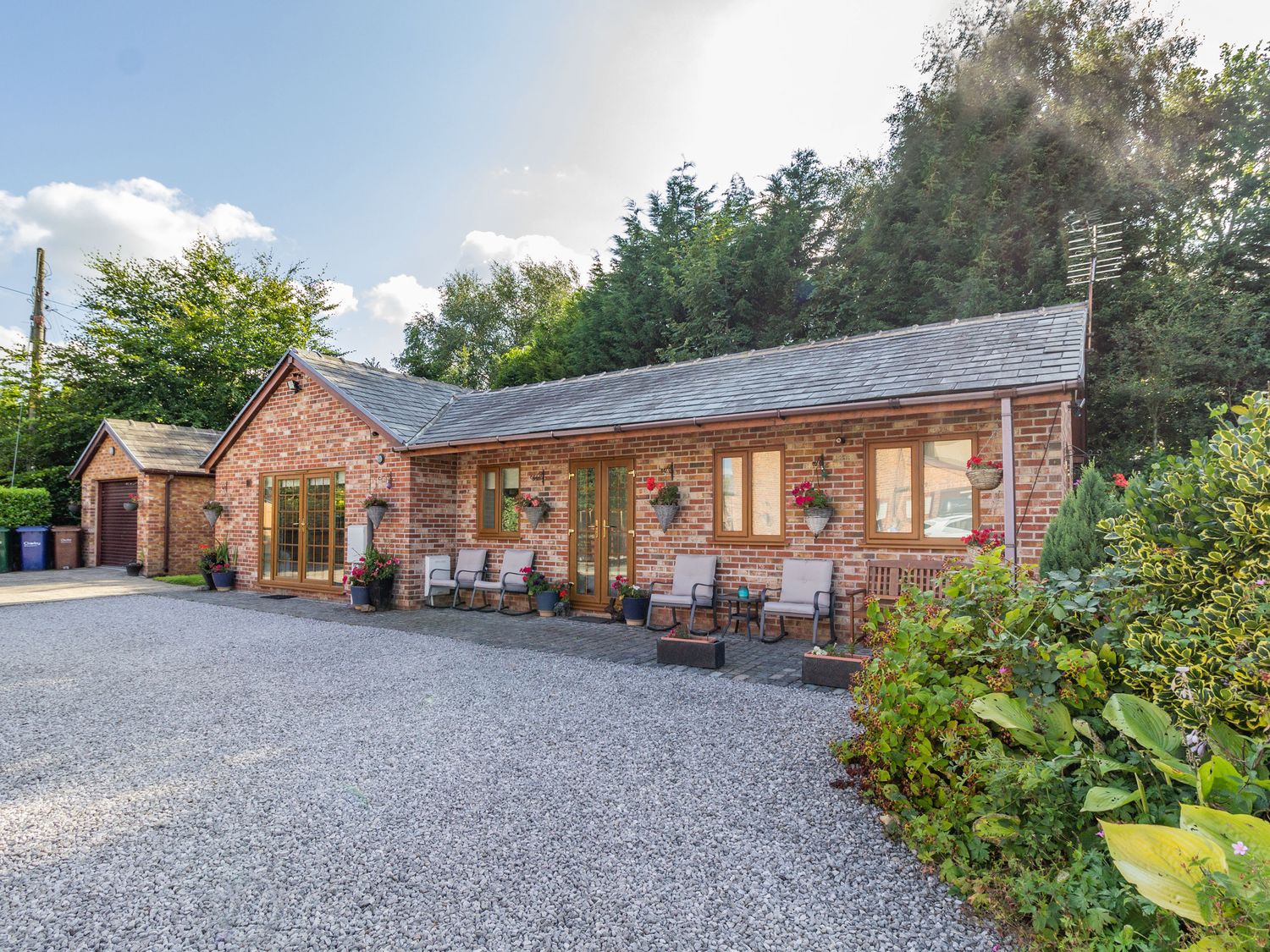 A brick house with large windows wooden framed doors chairs and plants on a gravel driveway with trees in the background at Wild Duck Lodge in Mawdesley near Southport