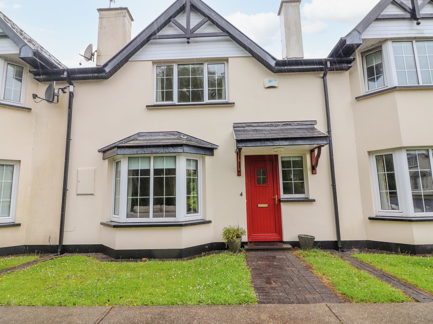 The front exterior of a house with a red door and two windows with a grass lawn at No 4 Lansdowne Village Kenmare The Ring of Kerry County Kerry