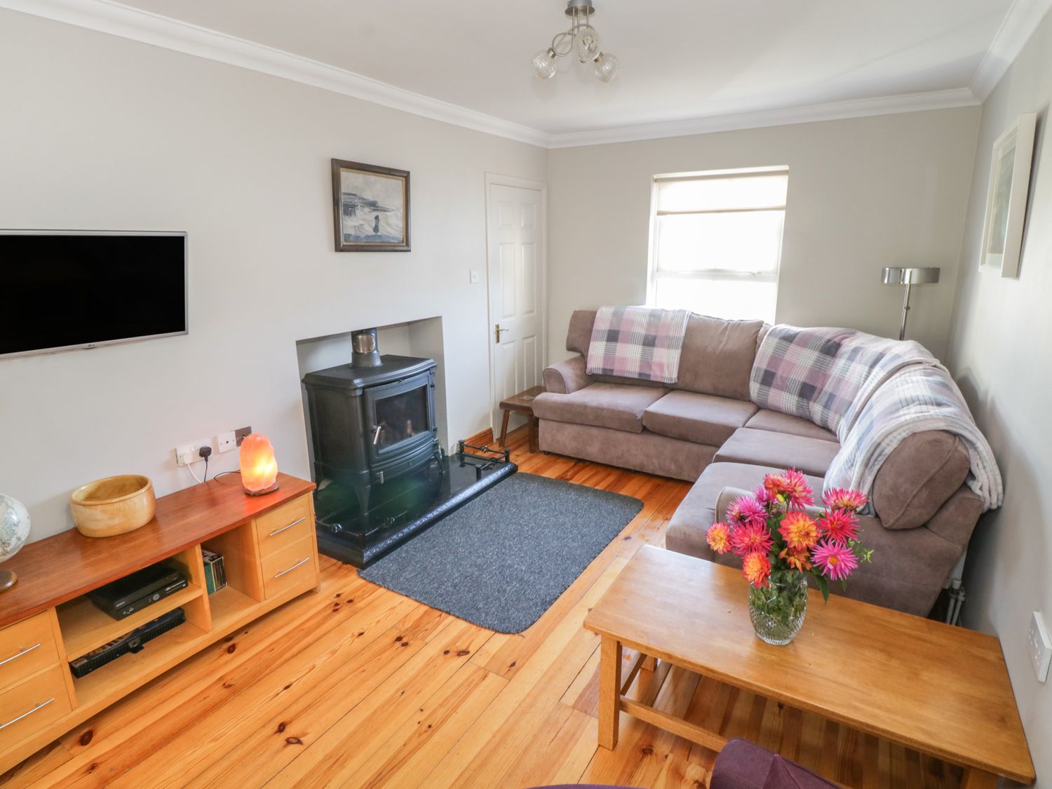 A living room with a sectional sofa and wooden coffee table with flowers a wood stove and a wooden media unit at Teach Teolai in Carraroe County Galway
