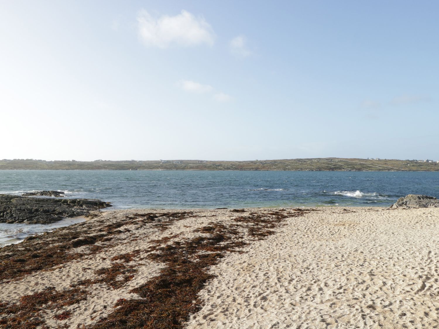 A sandy beach with seaweed near the ocean and a rocky shoreline at Teach Teolai in Carraroe County Galway