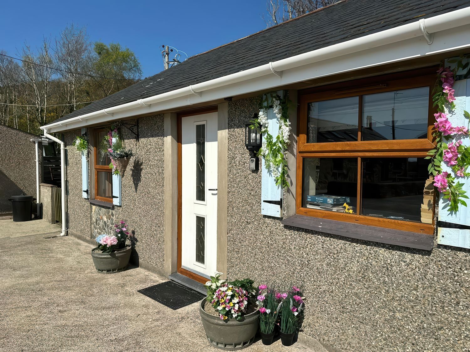 Exterior view of a house with a white door two windows blue shutters and flower pots at The Mill in Abererch near Pwllheli