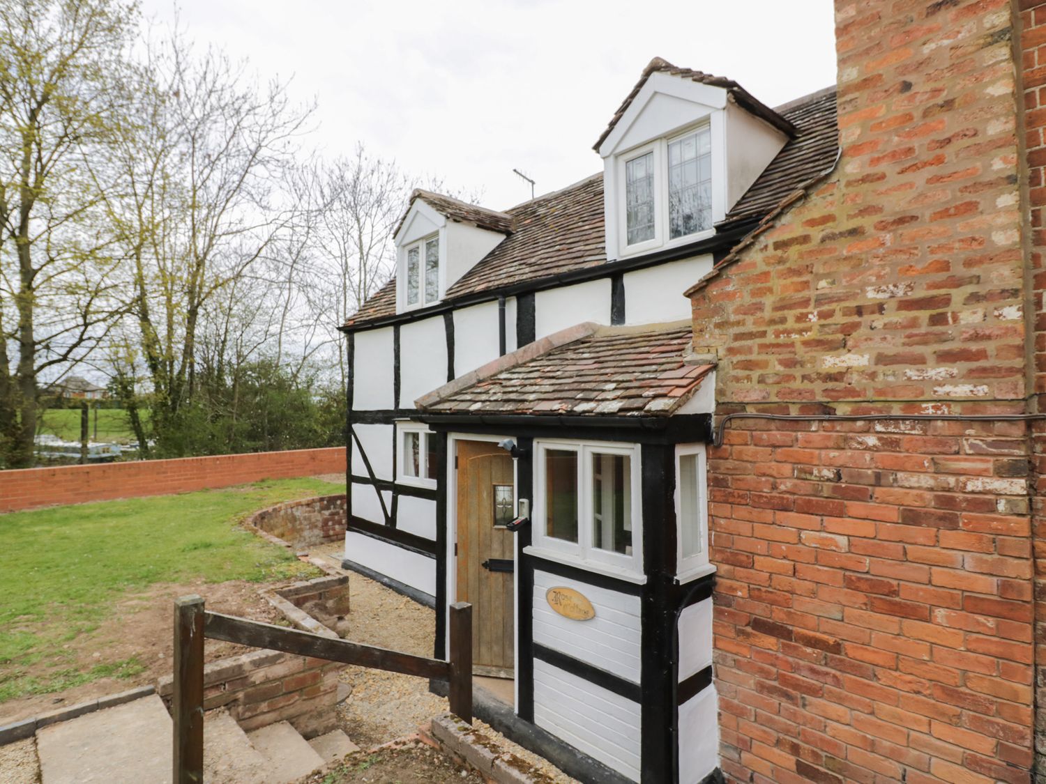 Exterior view of a black and white timber framed cottage with brick chimney and a small wooden door at Rose Cottage in Upton upon Severn