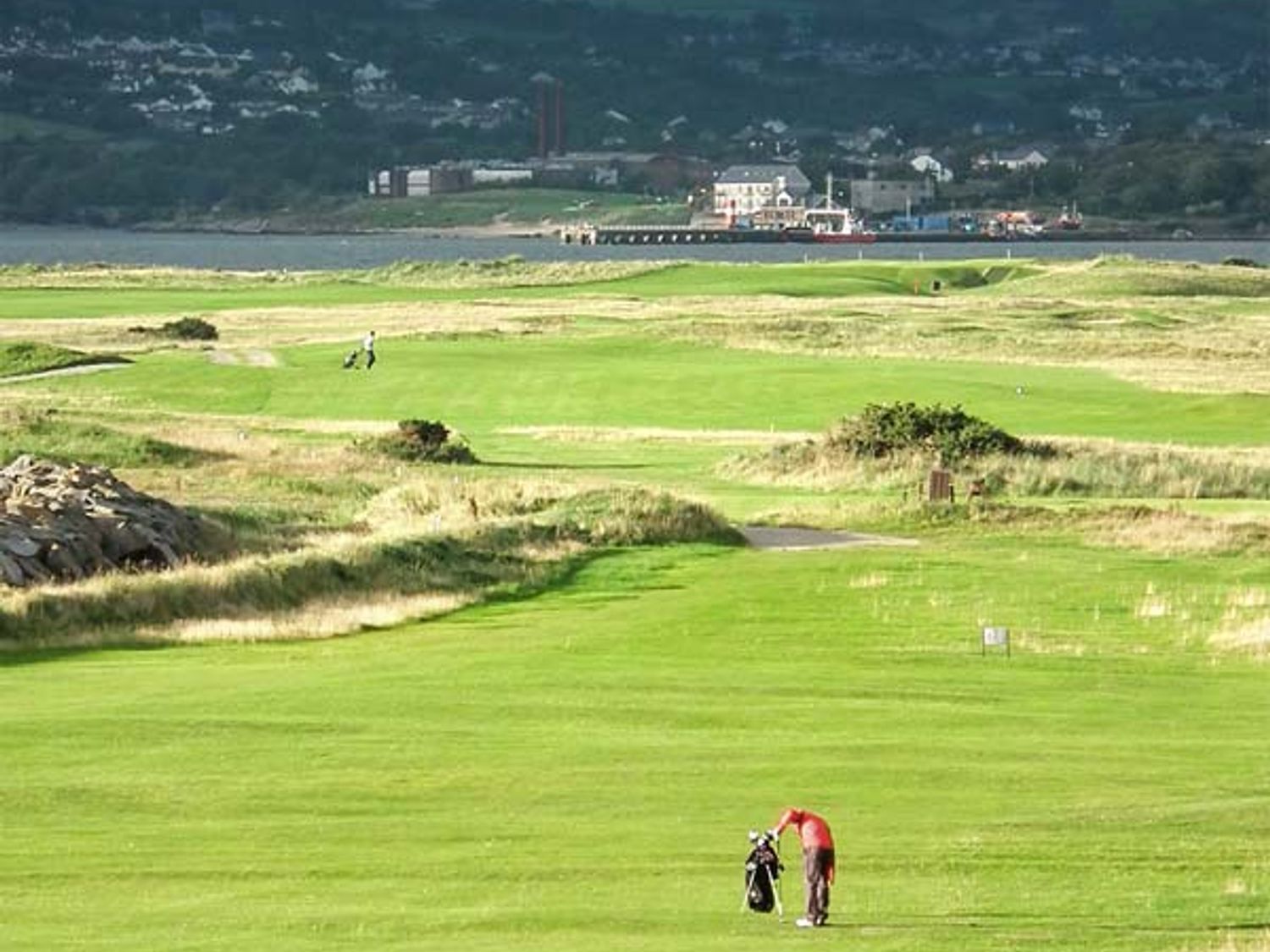 A golf course with two golfers and a body of water with buildings in the background at The Beach House Apartment in Buncrana County Donegal