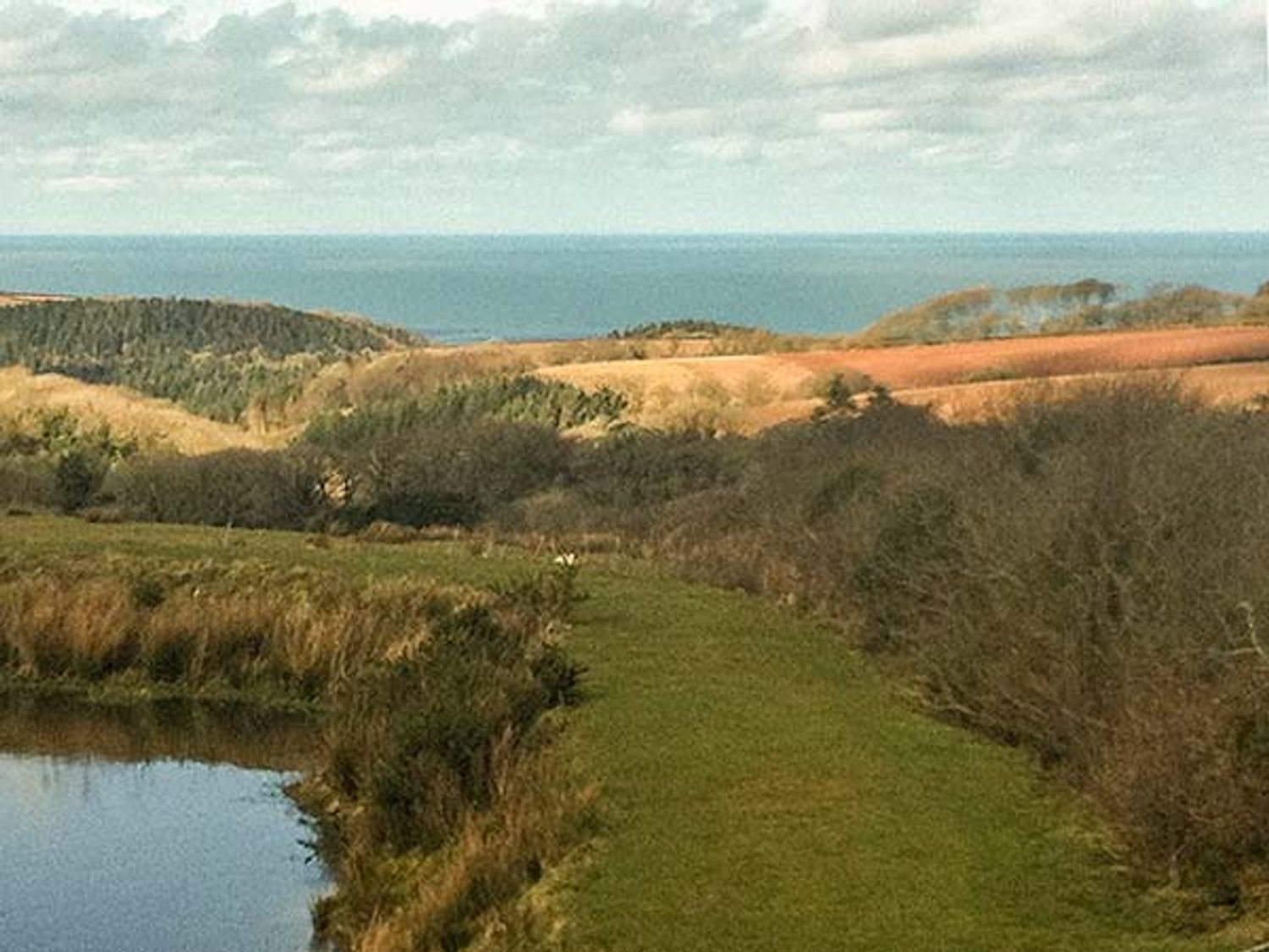 A landscape with a river a grassy path and hills with the sea in the background at Old Chapel Clovelly