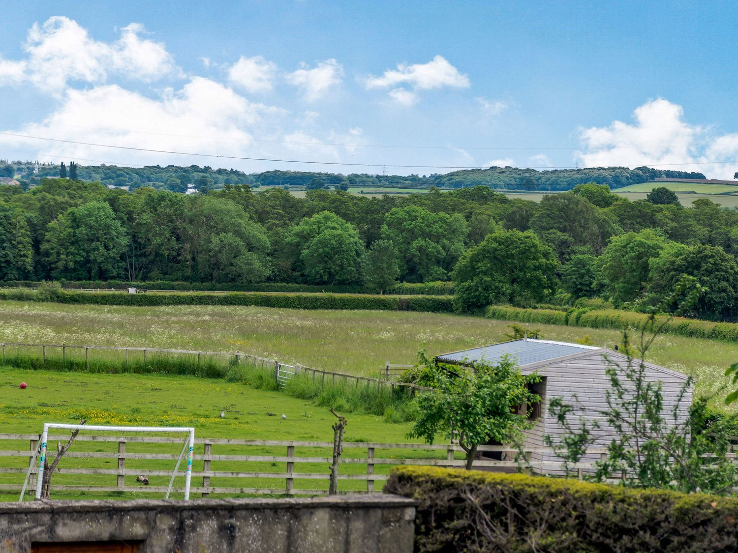 A grassy fenced field with a small wooden shed and a soccer goal post at Snowdrop Cottage in Clifford West Yorkshire