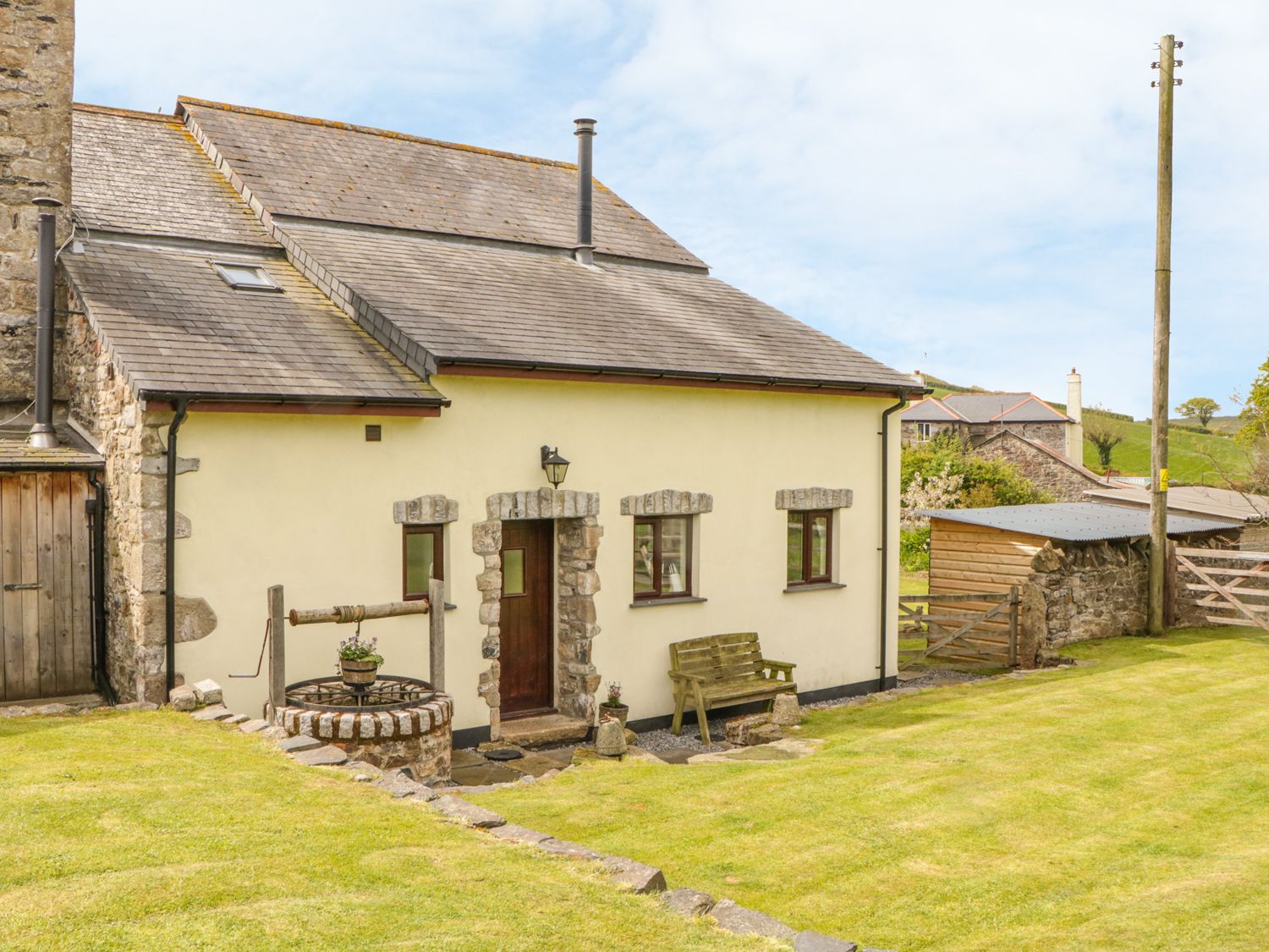 A stone and cream colored house with a wooden door stone framed windows a wooden bench and a stone well in a grass yard at Higher Whiddon Farm Whiddon Well Ashburton near Newton Abbot