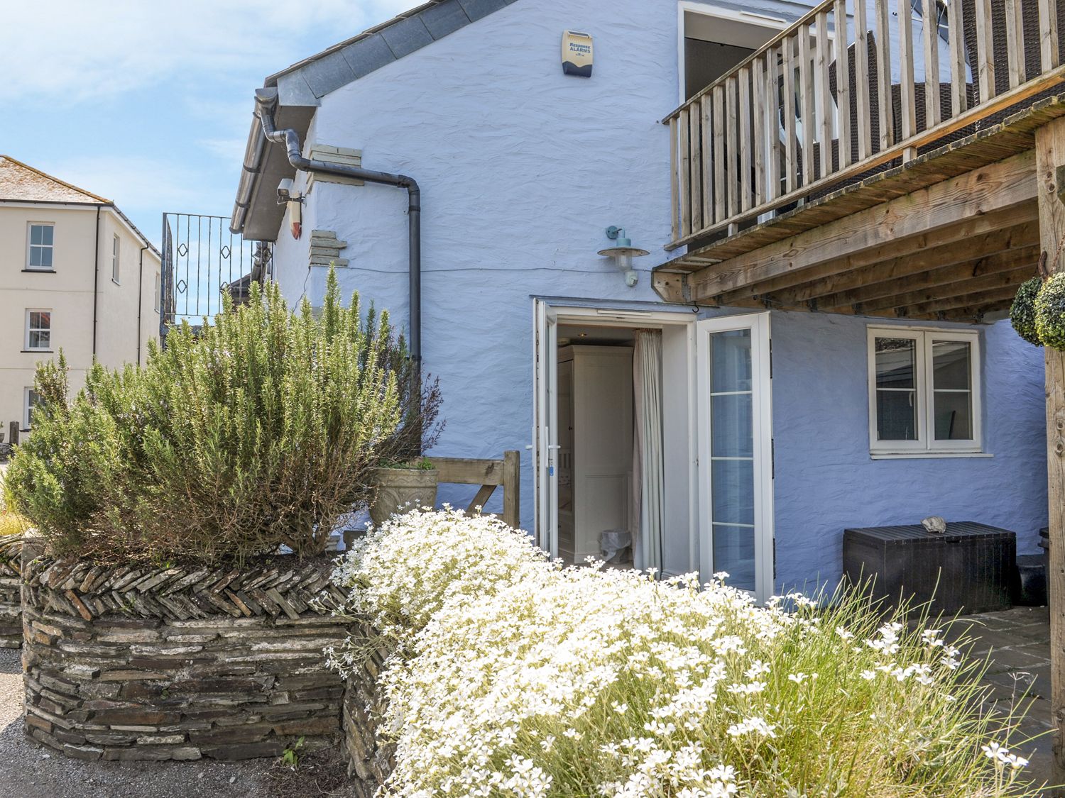 The exterior of a blue house with a wooden balcony stone planters with green bushes and white flowers at The Blue House in Tintagel