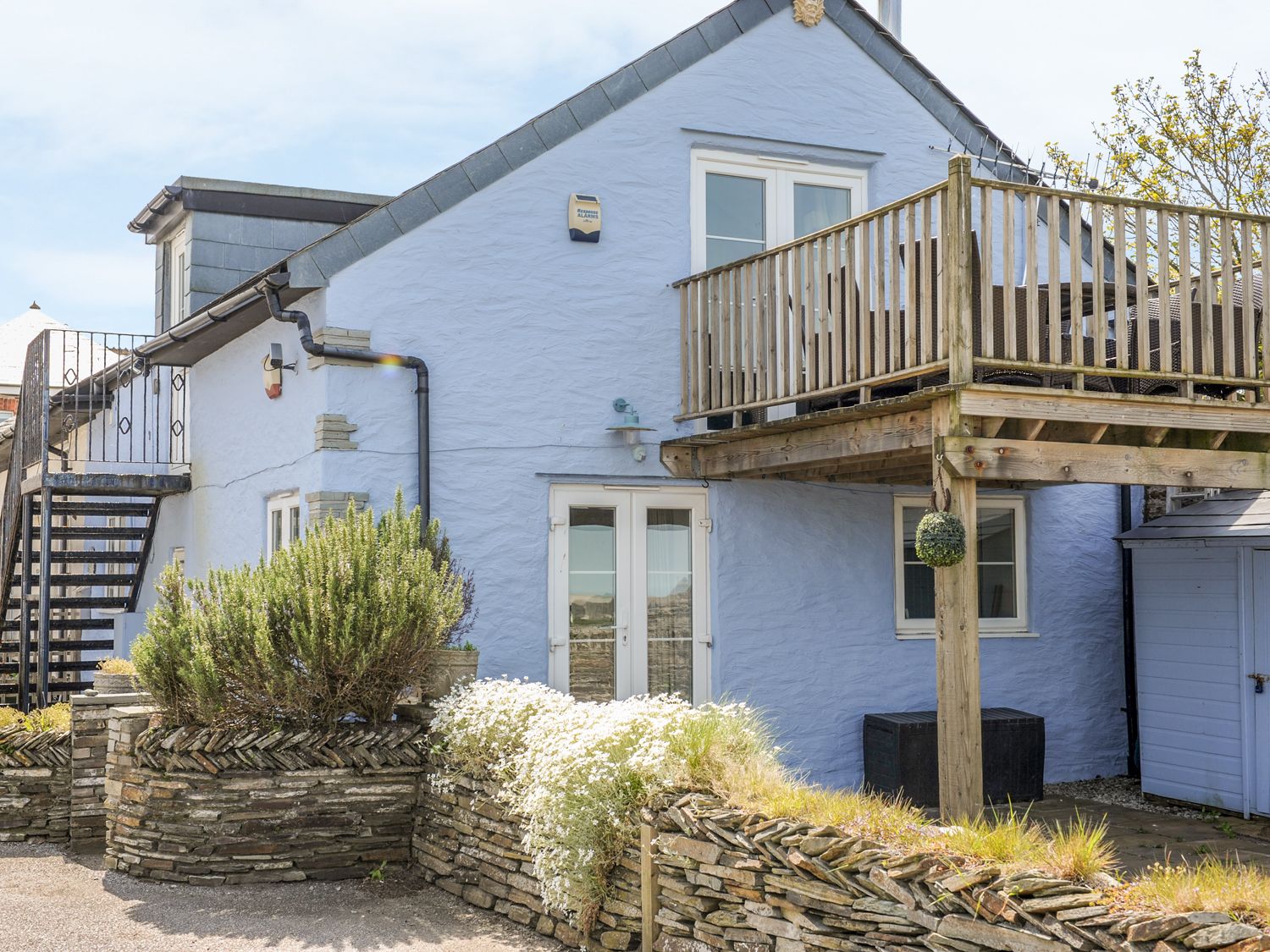 A blue house with stone planters and a wooden balcony with outdoor furniture at The Blue House in Tintagel