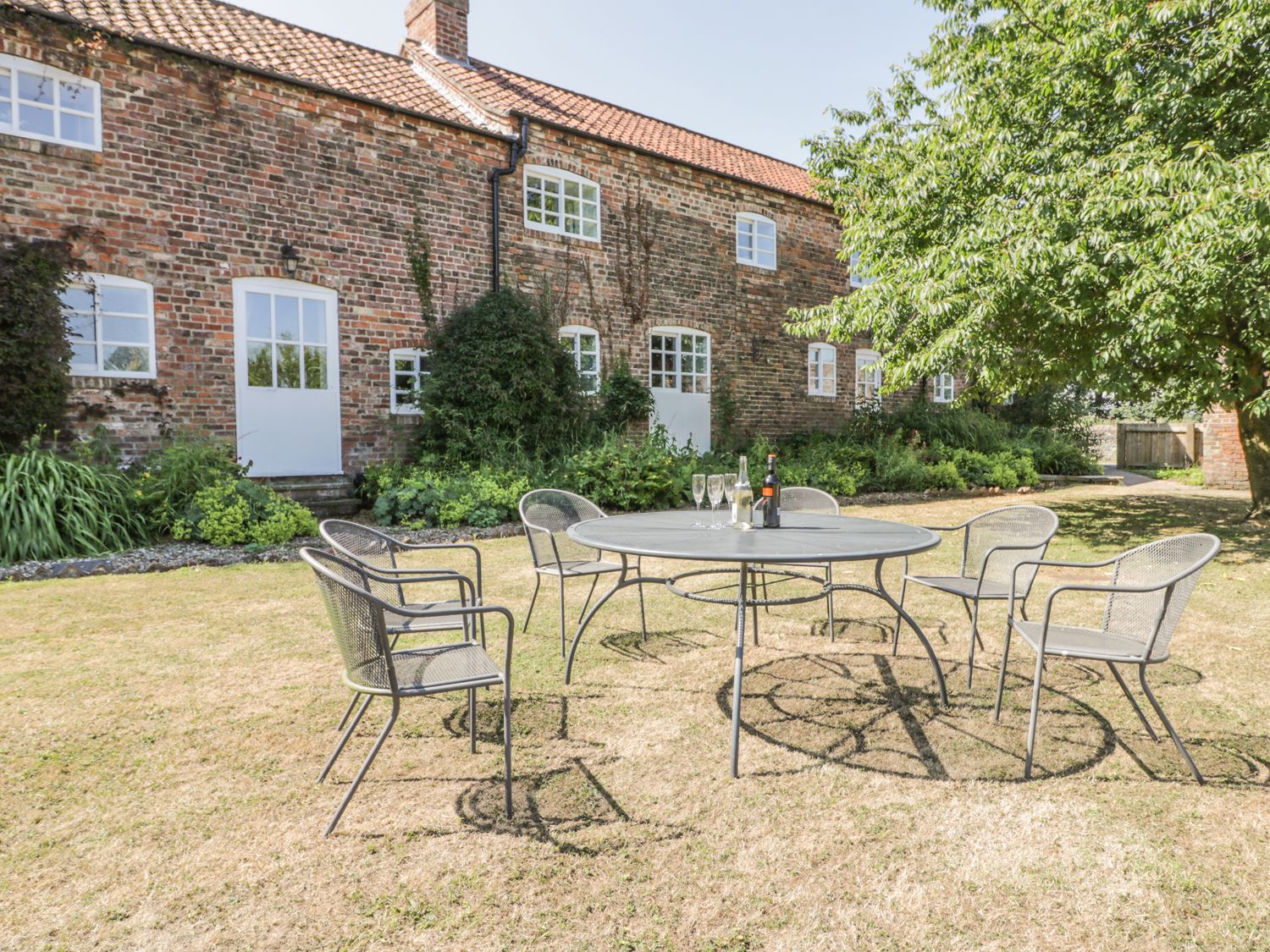 A garden with a round metal table and six chairs outside a brick building at Bramhill Barns in Burton Pidsea