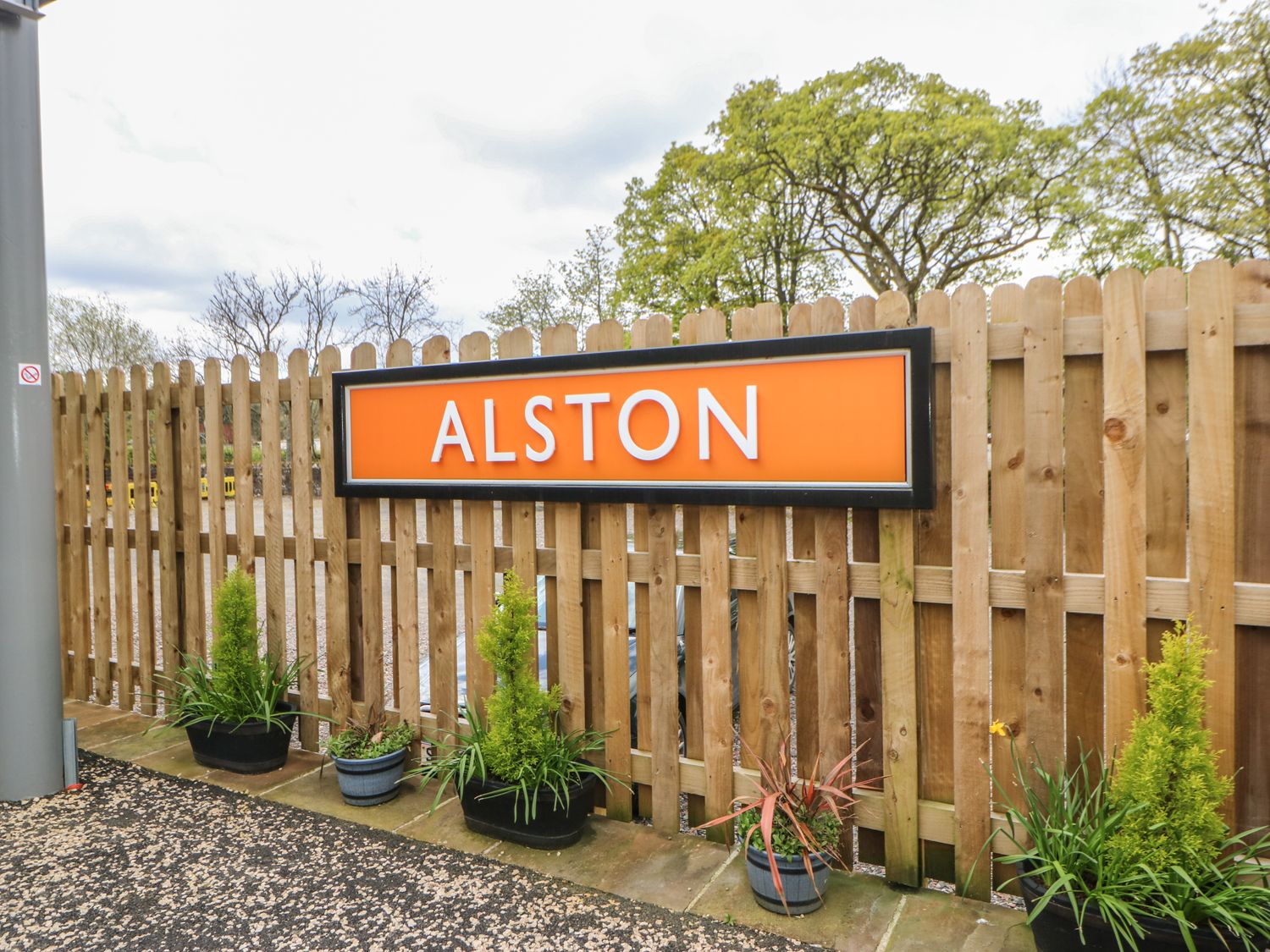 An orange sign with the word Alston on a wooden fence with potted plants in front at The Hayloft in Alston