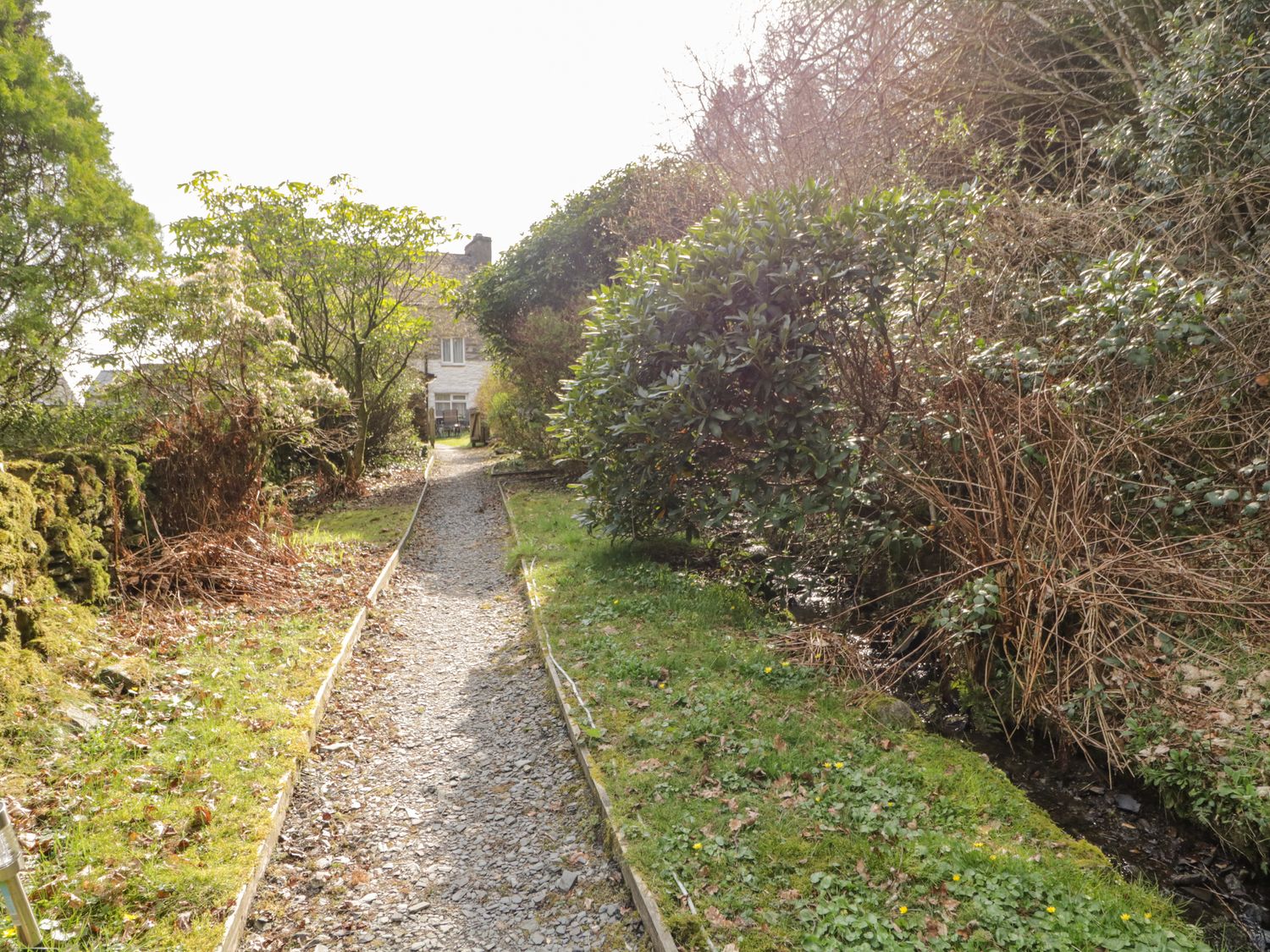A gravel path bordered by grass and shrubs with a house visible in the background at Duddon Cottage in Broughton-in-Furness