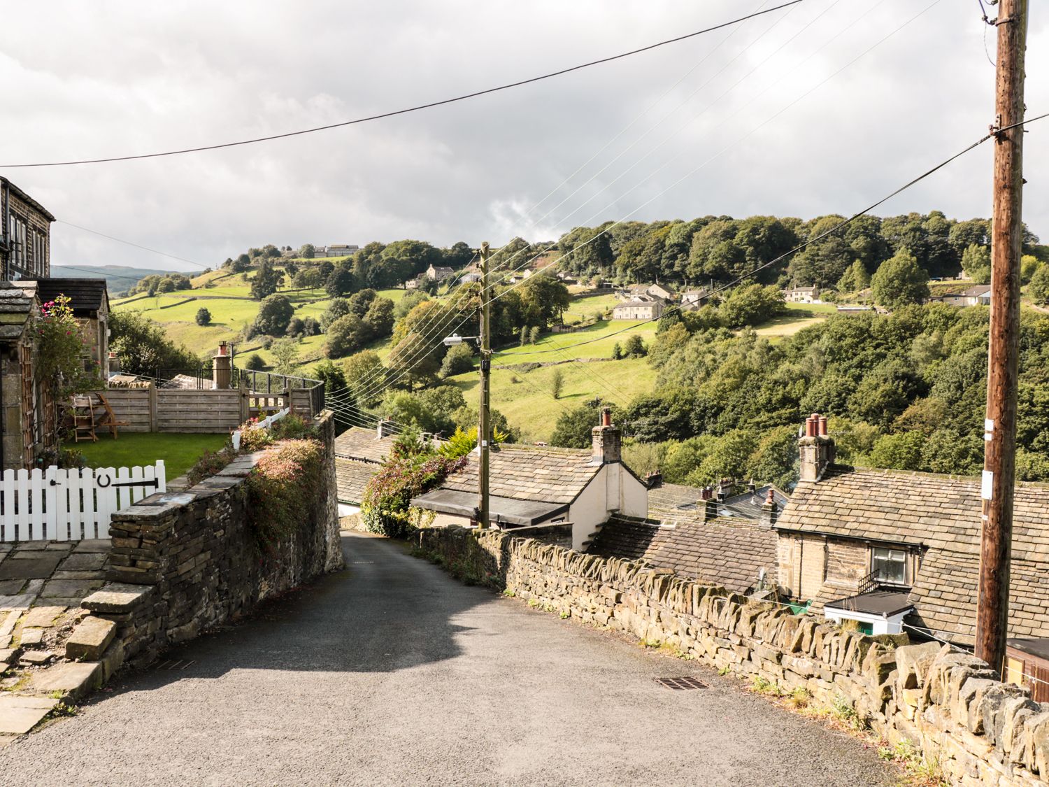 A sloped road with stone walls and houses surrounded by green hills and trees in a rural area