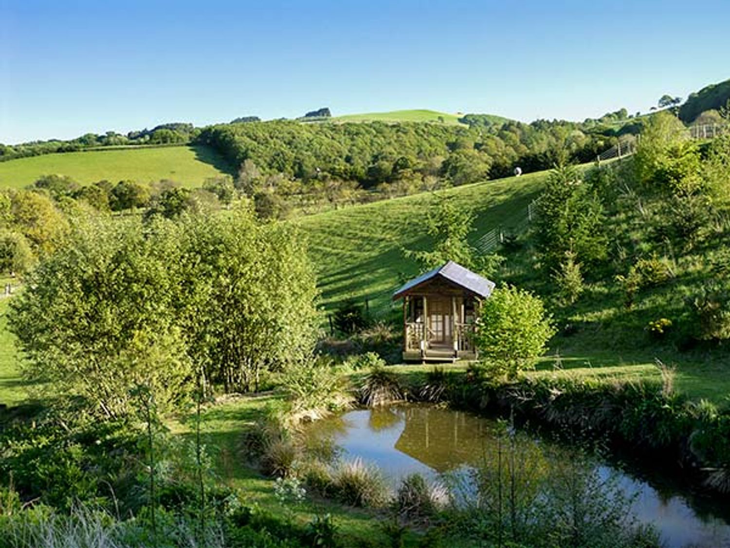 A small wooden cabin near a pond with trees and hills in the background at Black Mountain View in Llanafan Fawr near Builth Wells