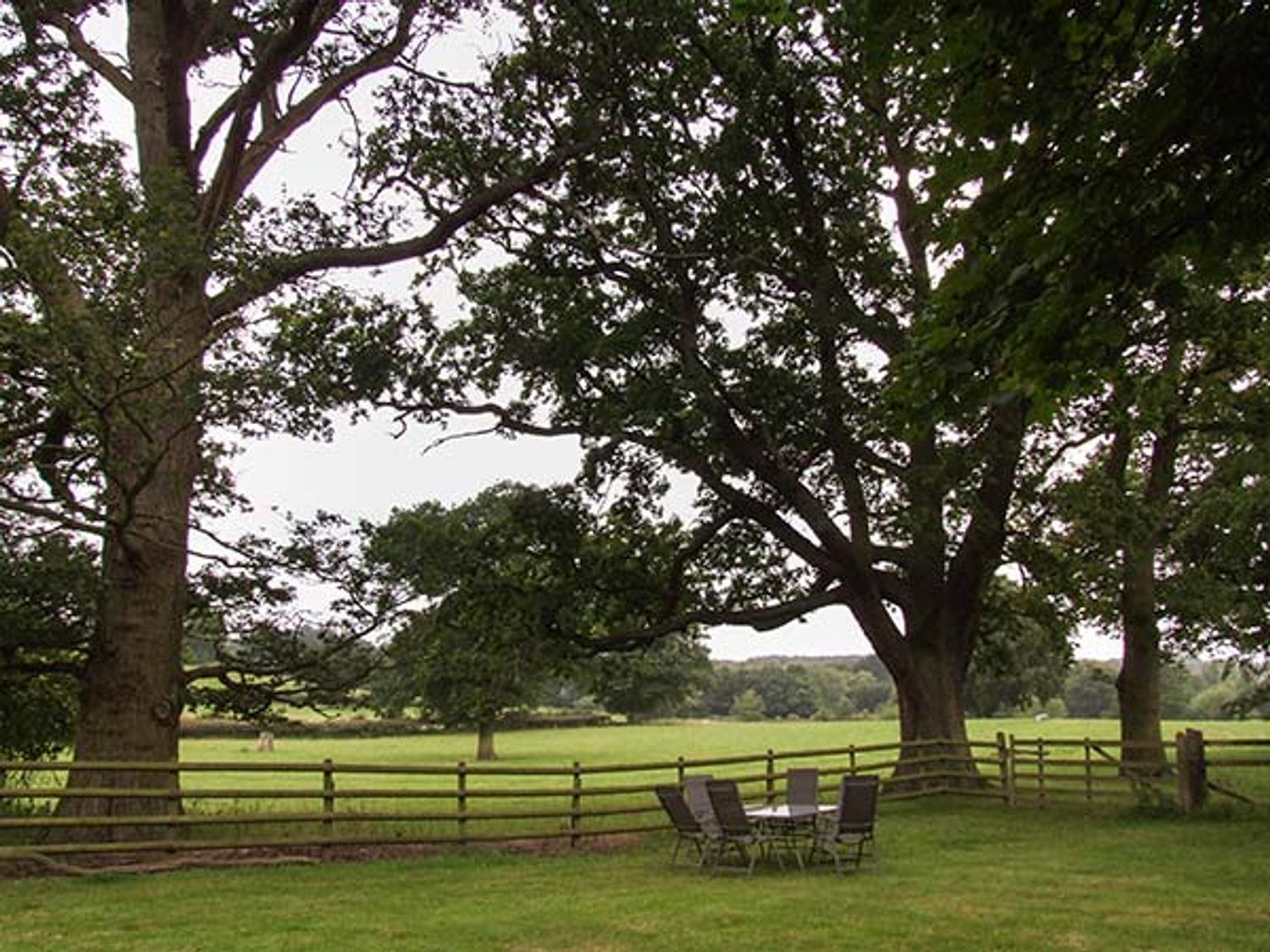 A grassy yard with a wooden fence trees and a patio table with six chairs at Finwood Cottage 1 in Rowington