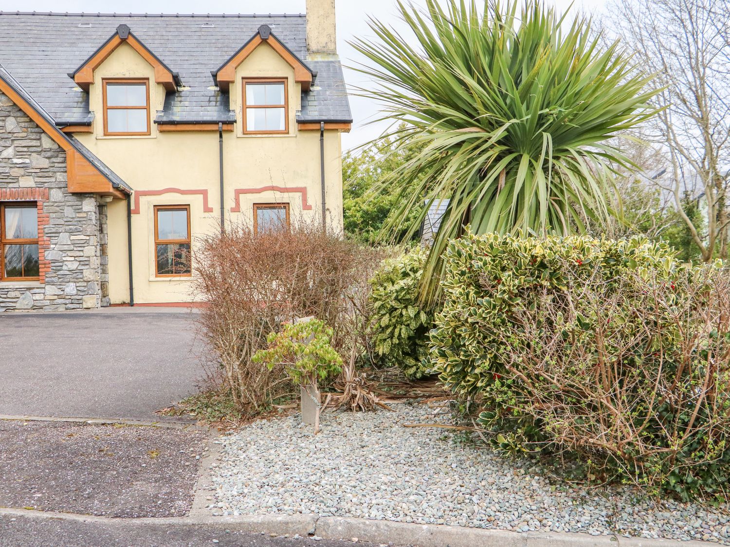 A house with stone and yellow walls with windows and a gravel area with plants and bushes in front at Kenmare Bay Cottage in Kenmare County Kerry