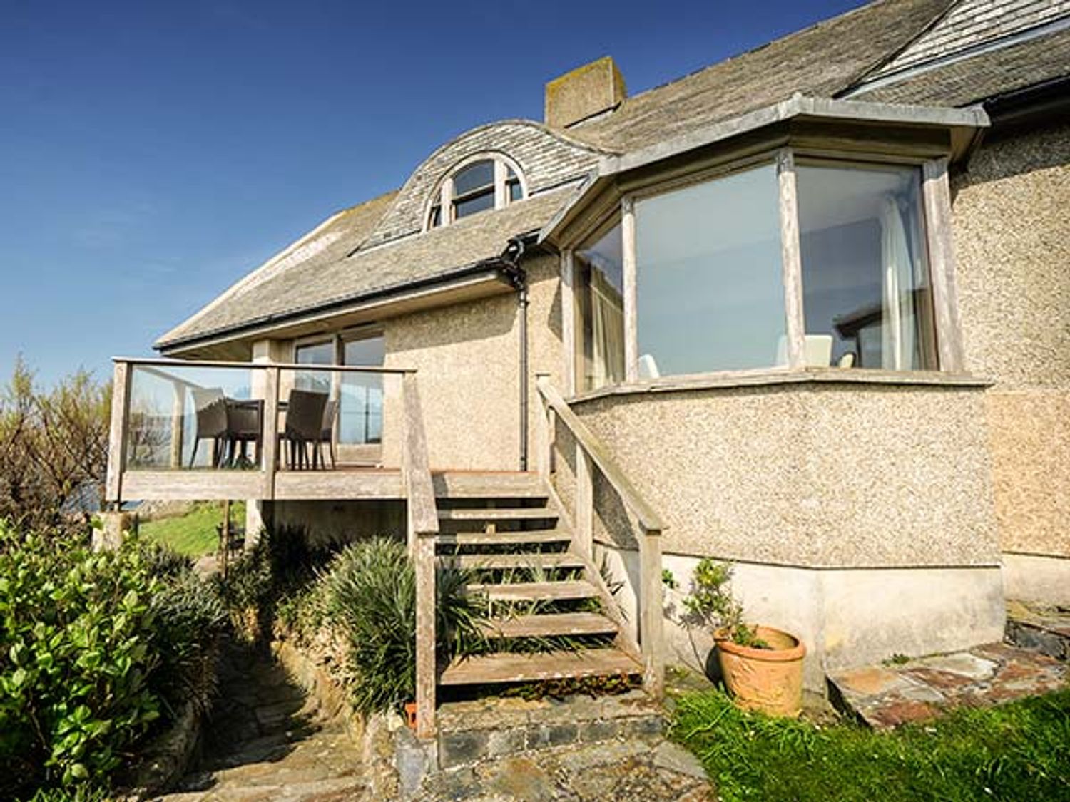 Exterior view of a house with a wooden staircase leading to a small balcony with chairs and a table at Cragford in Sennen Cove