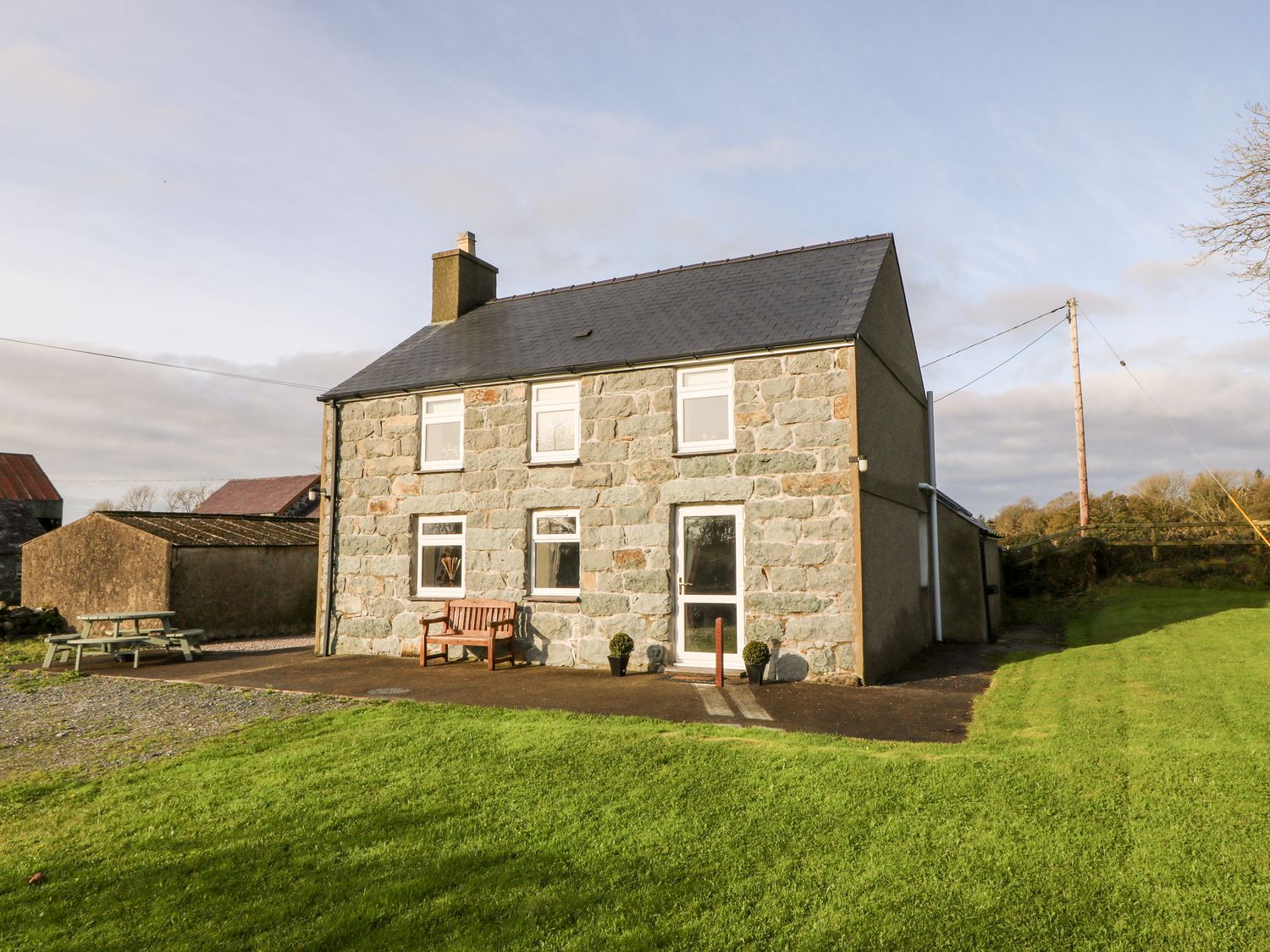 A stone house with six windows a bench and two potted plants on a lawn at Prys Mawr in Chwilog near Criccieth