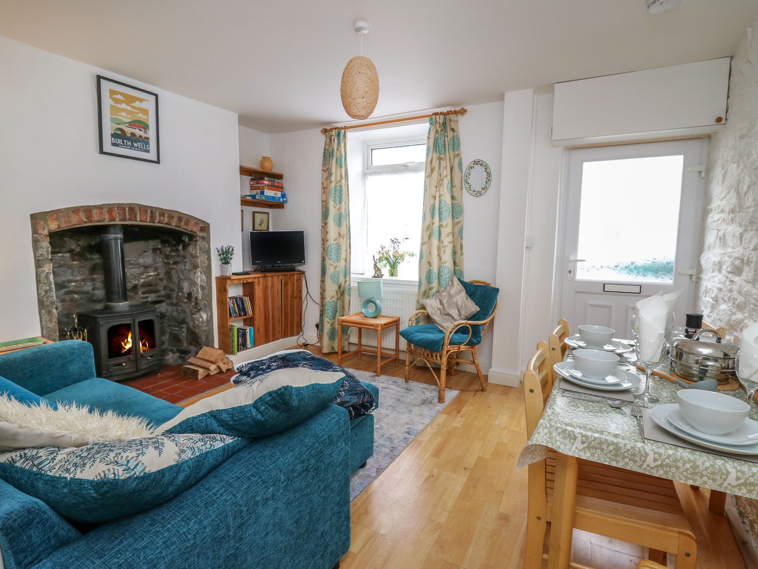 A living room with a fireplace a blue sofa a wooden dining table set and a window with patterned curtains at Rowan Cottage in Builth Wells