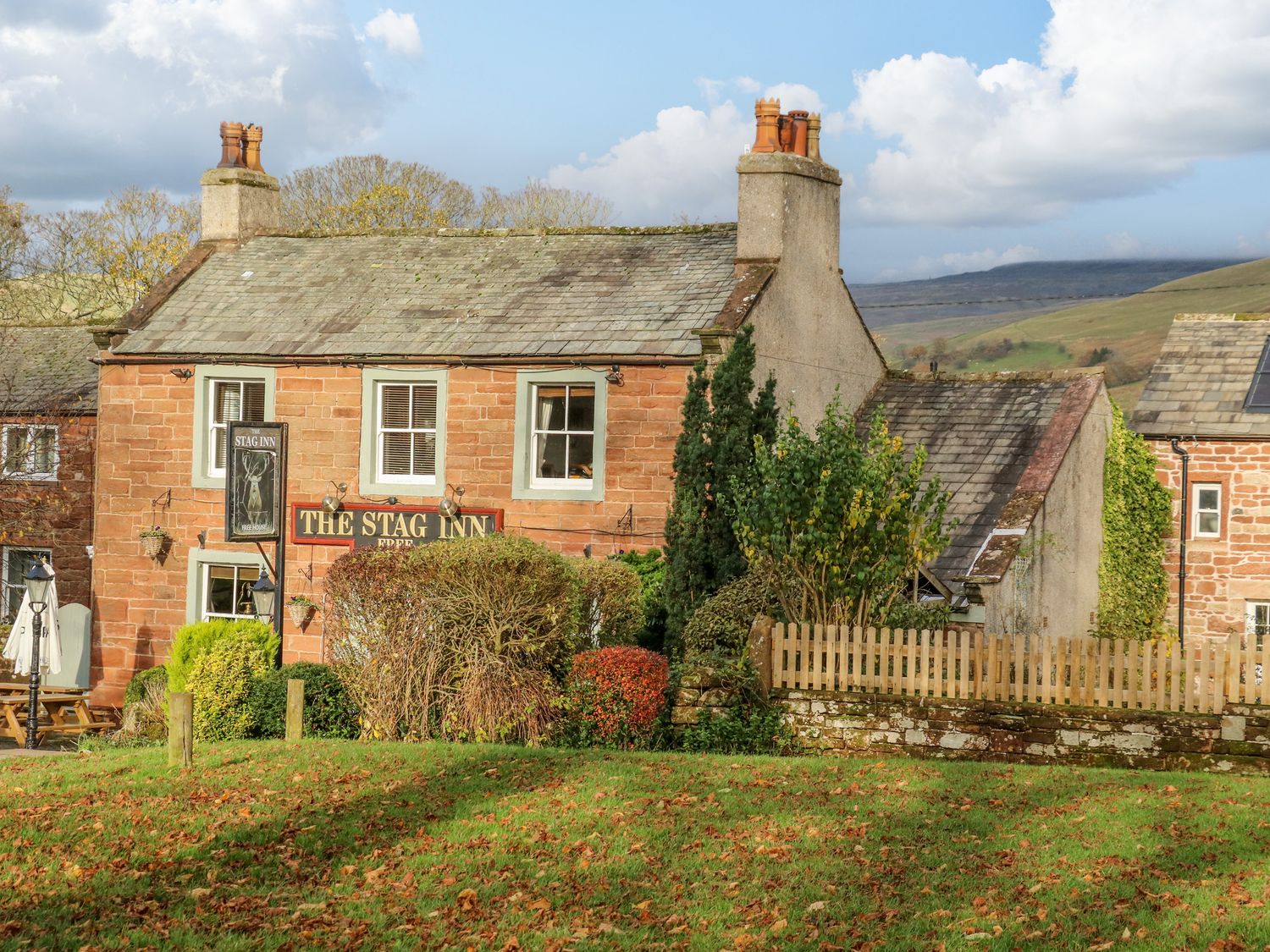 A stone building with a sign reading the stag inn surrounded by bushes and a lawn at Carwood in Dufton