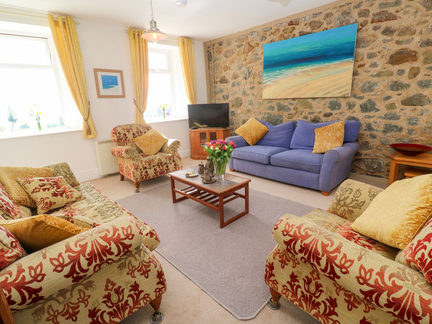 A living room with patterned armchairs sofa coffee table and a stone wall at Seaview in Coverack