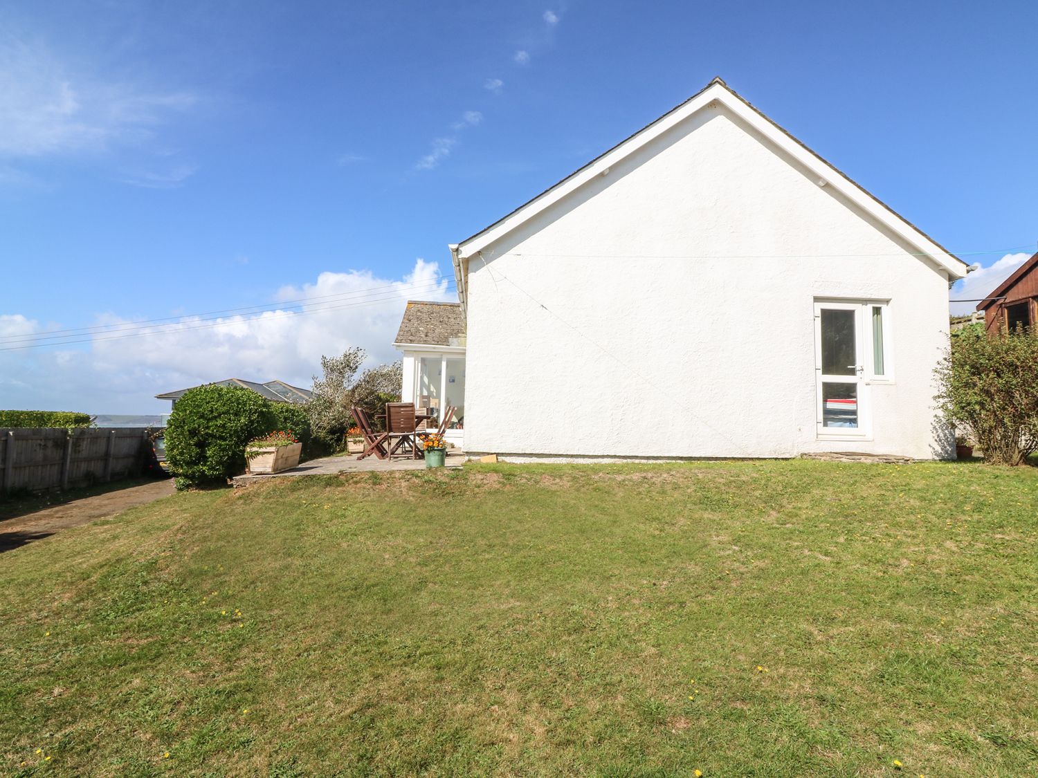 A white house with a grassy lawn and outdoor wooden chairs and table at Highdown in Bigbury on Sea near Modbury