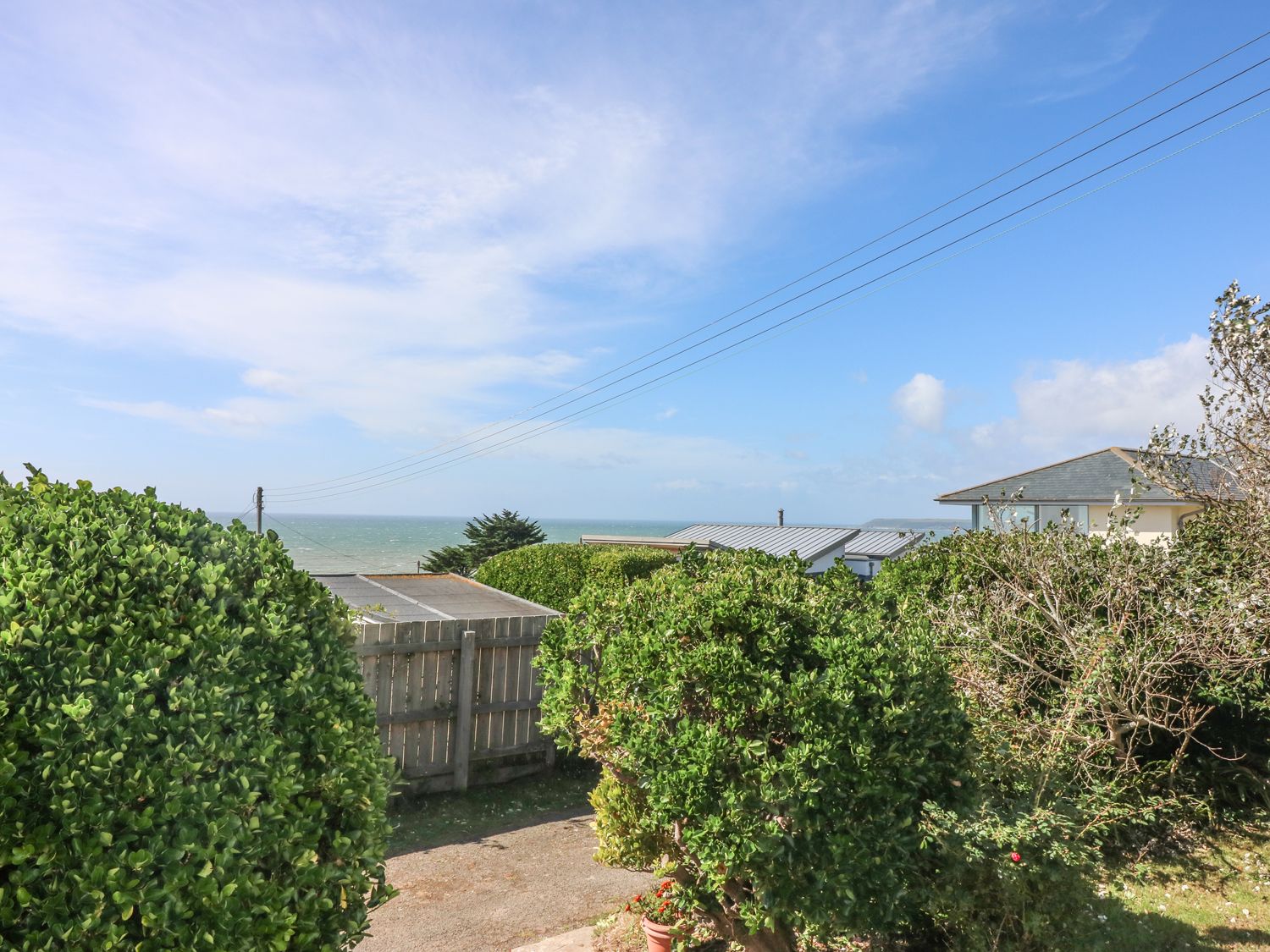 A garden with bushes and a wooden fence overlooking rooftops and the sea at Highdown in Bigbury on Sea near Modbury