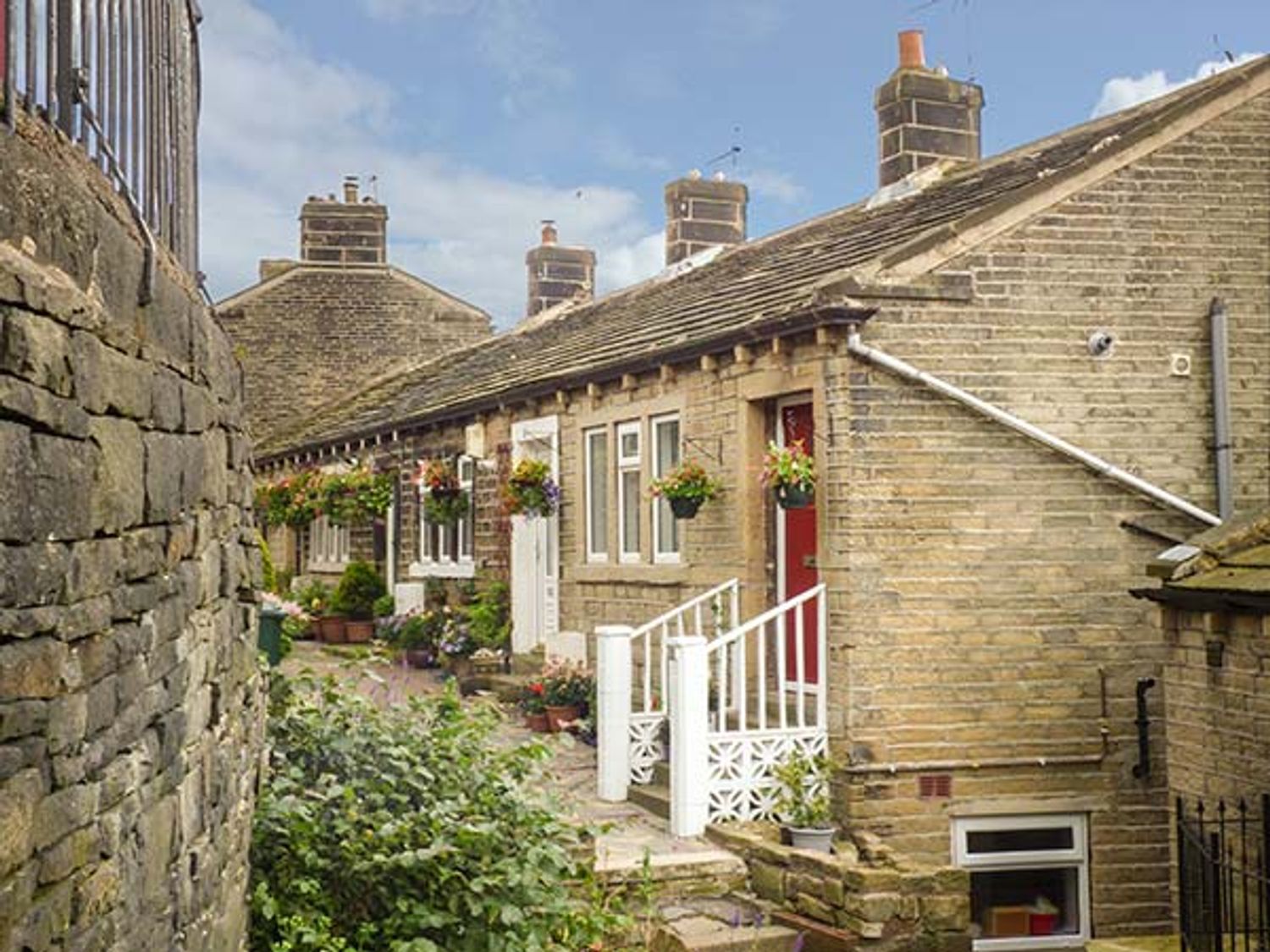 A row of brick terraced houses with hanging flower baskets and potted plants outside at Ginnel Corner in Golcar