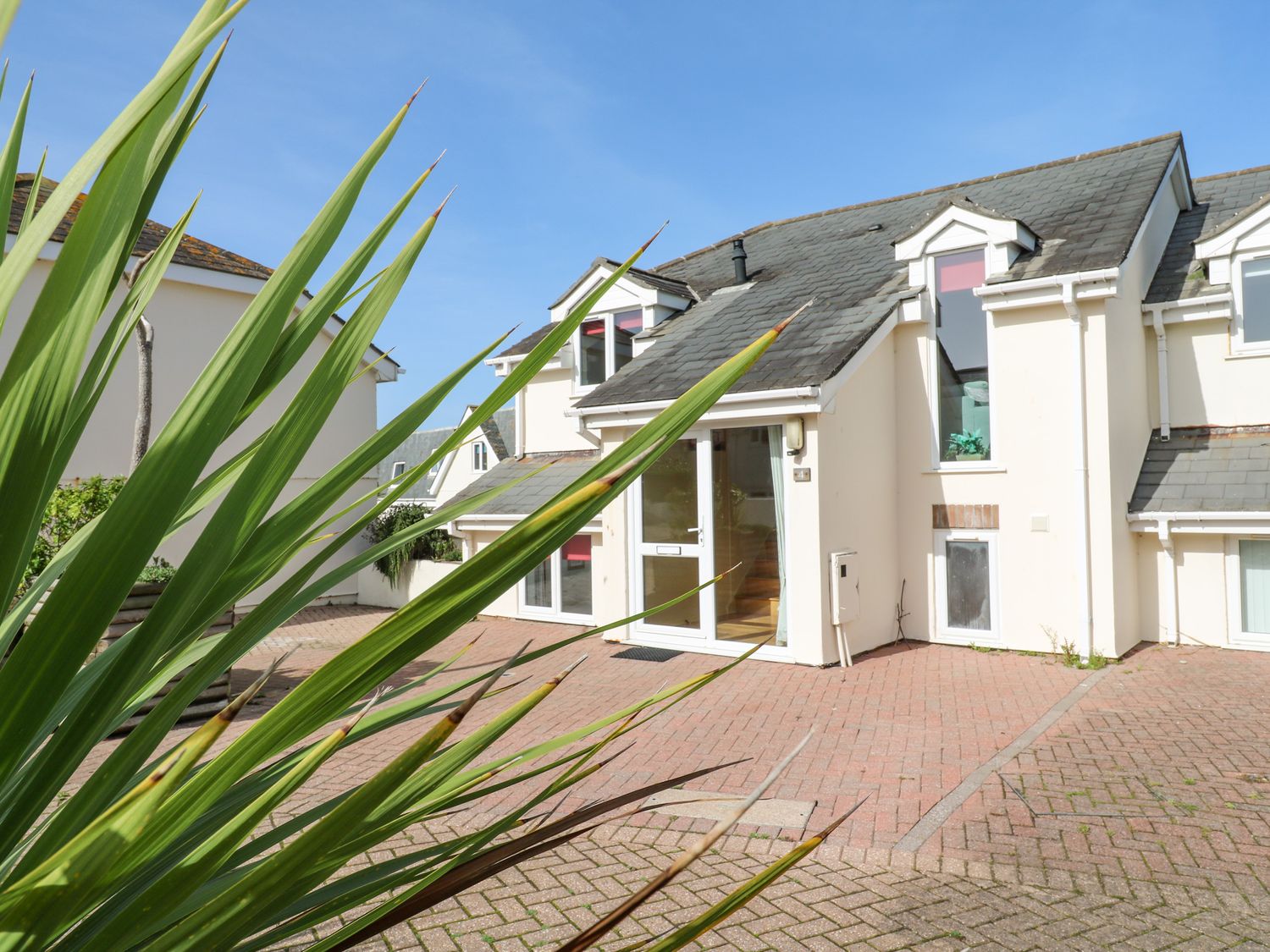 The exterior of a house with a tiled roof a glass door and large windows with a paved driveway and plants in view at The Beach House in Porth near Newquay